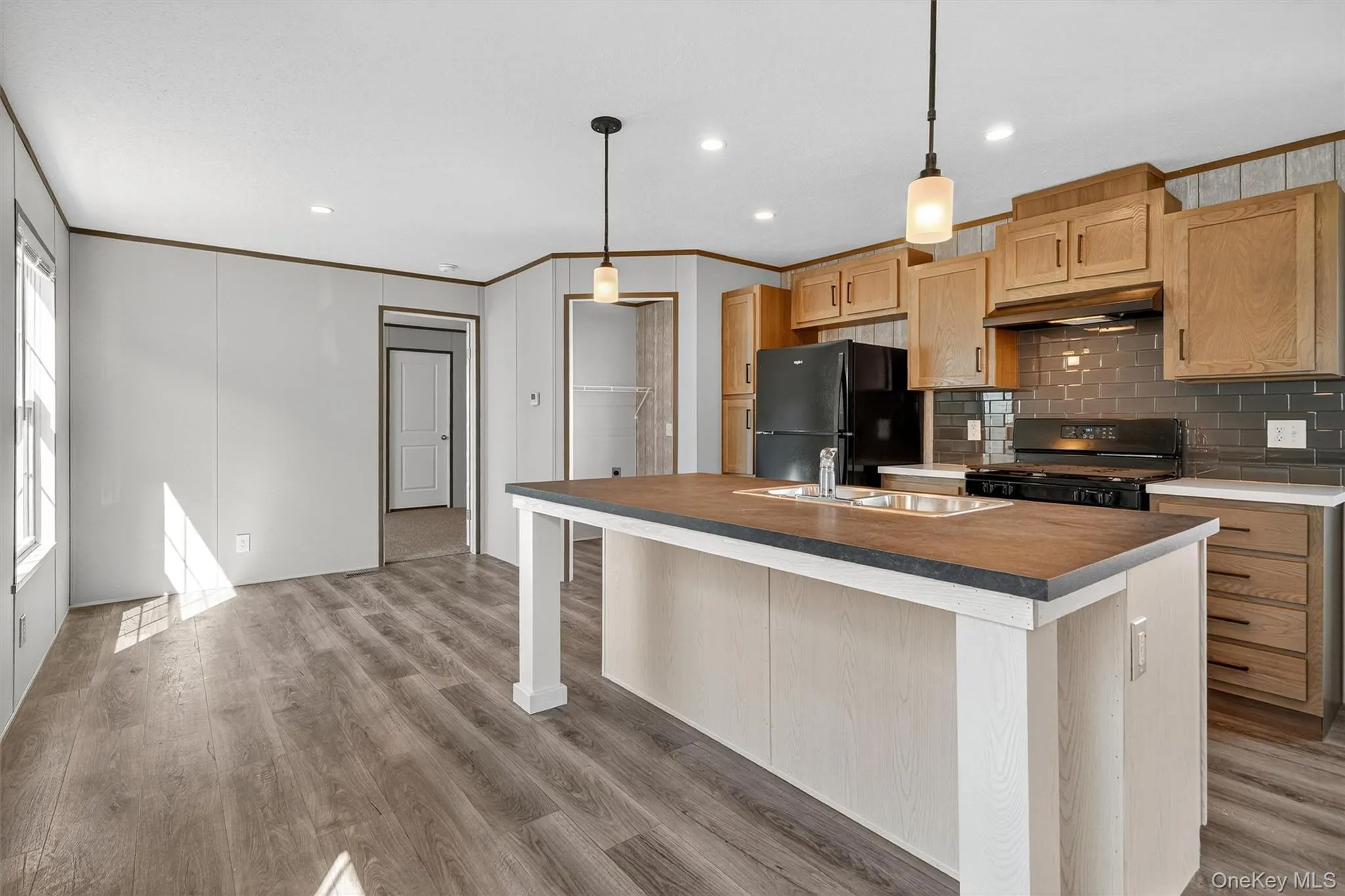 Kitchen with ornamental molding, decorative backsplash, light brown cabinets, an island with sink, and black appliances Kitchen with ornamental molding, decorative backsplash, light brown cabinets, an island with sink, and black appliances