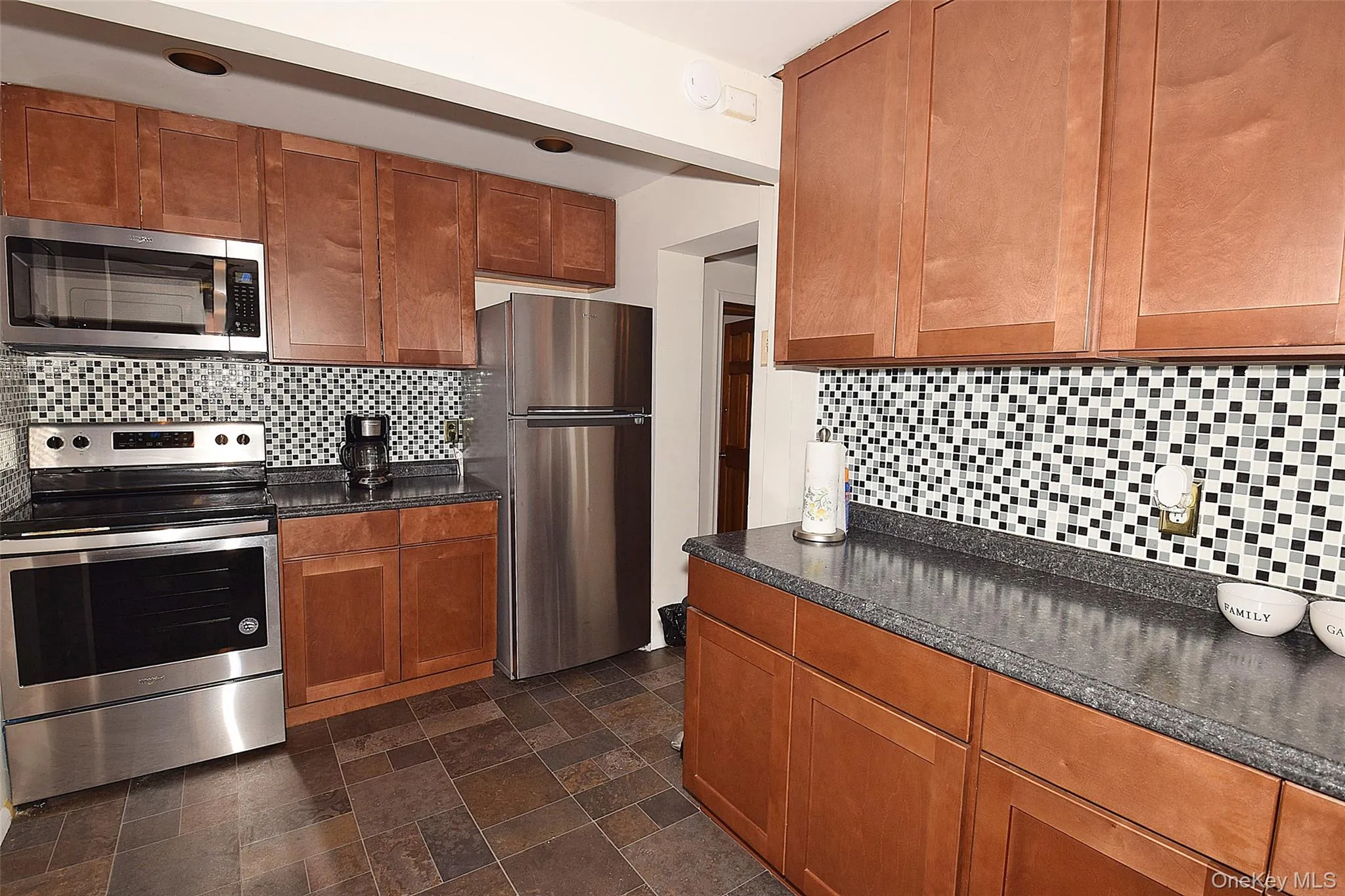 Kitchen with stainless steel appliances, decorative backsplash, stone finish floor, and brown cabinets Kitchen with stainless steel appliances, decorative backsplash, stone finish floor, and brown cabinets