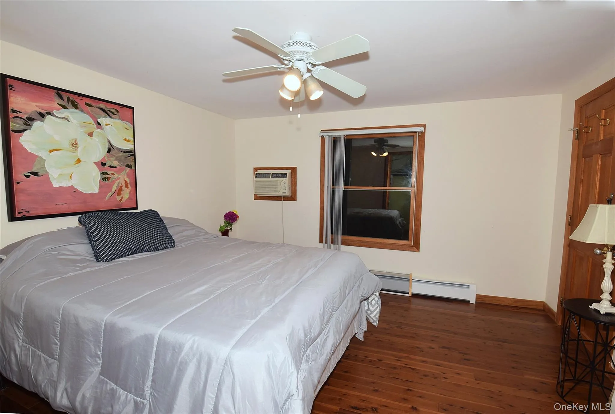 Bedroom with wood finished floors, baseboards, ceiling fan, a baseboard radiator, and a wall mounted AC Bedroom with wood finished floors, baseboards, ceiling fan, a baseboard radiator, and a wall mounted AC
