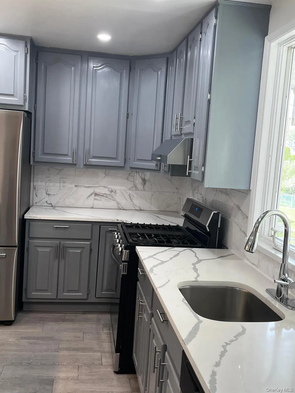 Kitchen featuring grey cabinetry, white countertops with grey veining, a stainless steel sink with a gooseneck faucet, a black range, and wood-finish flooring Kitchen featuring grey cabinetry, white countertops with grey veining, a stainless steel sink with a gooseneck faucet, a black range, and wood-finish flooring