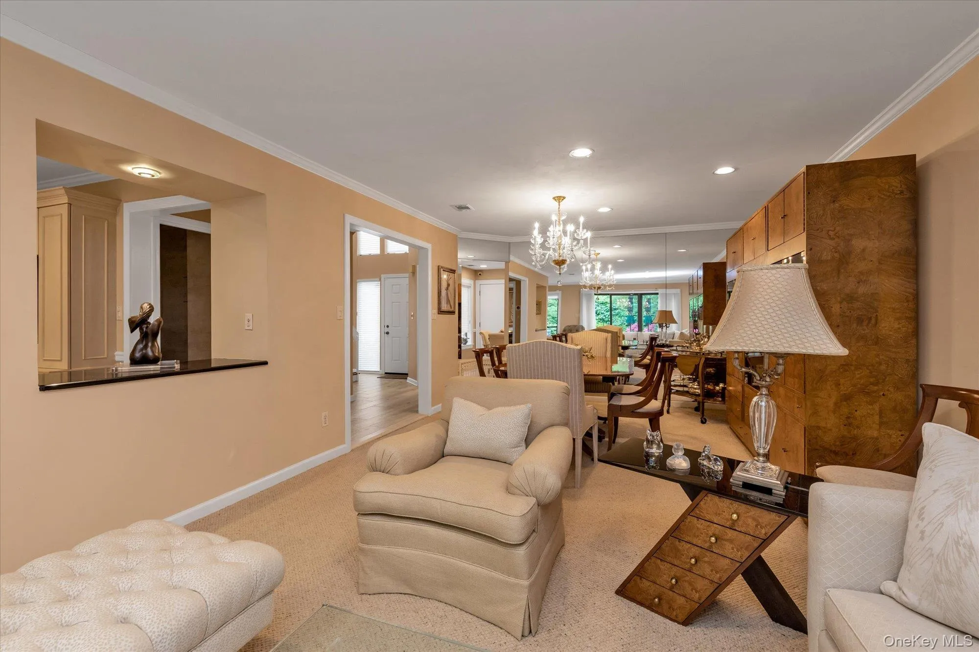 Spacious interior featuring a passthrough window with a dark countertop, crown molding, light-colored carpeting, and a built-in wood storage unit Spacious interior featuring a passthrough window with a dark countertop, crown molding, light-colored carpeting, and a built-in wood storage unit
