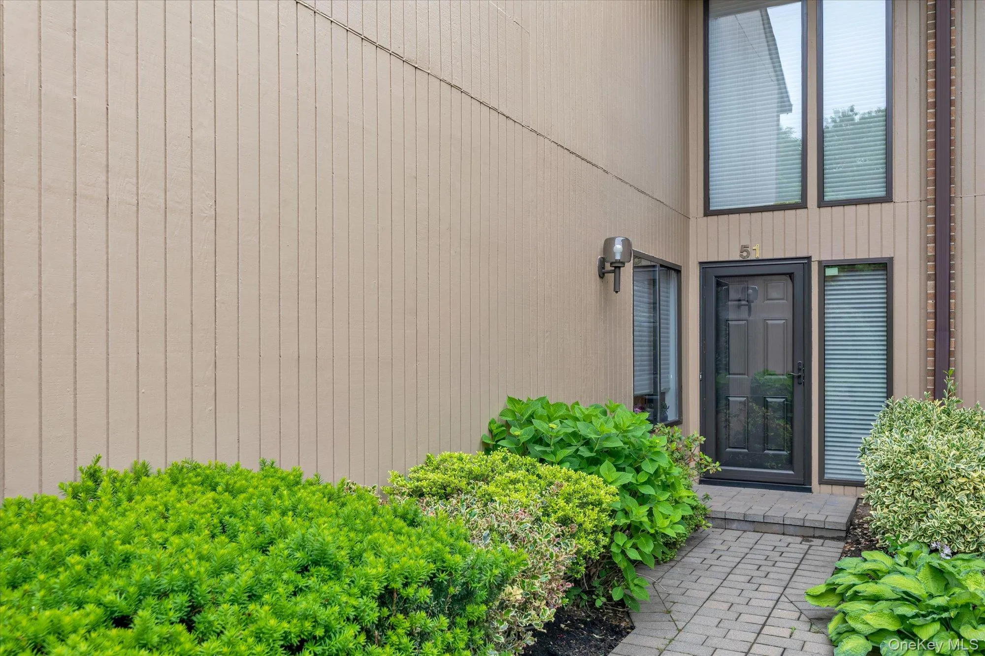 Entryway featuring vertical plank siding, a dark paneled door with glass insert, and a stone paver walkway Entryway featuring vertical plank siding, a dark paneled door with glass insert, and a stone paver walkway