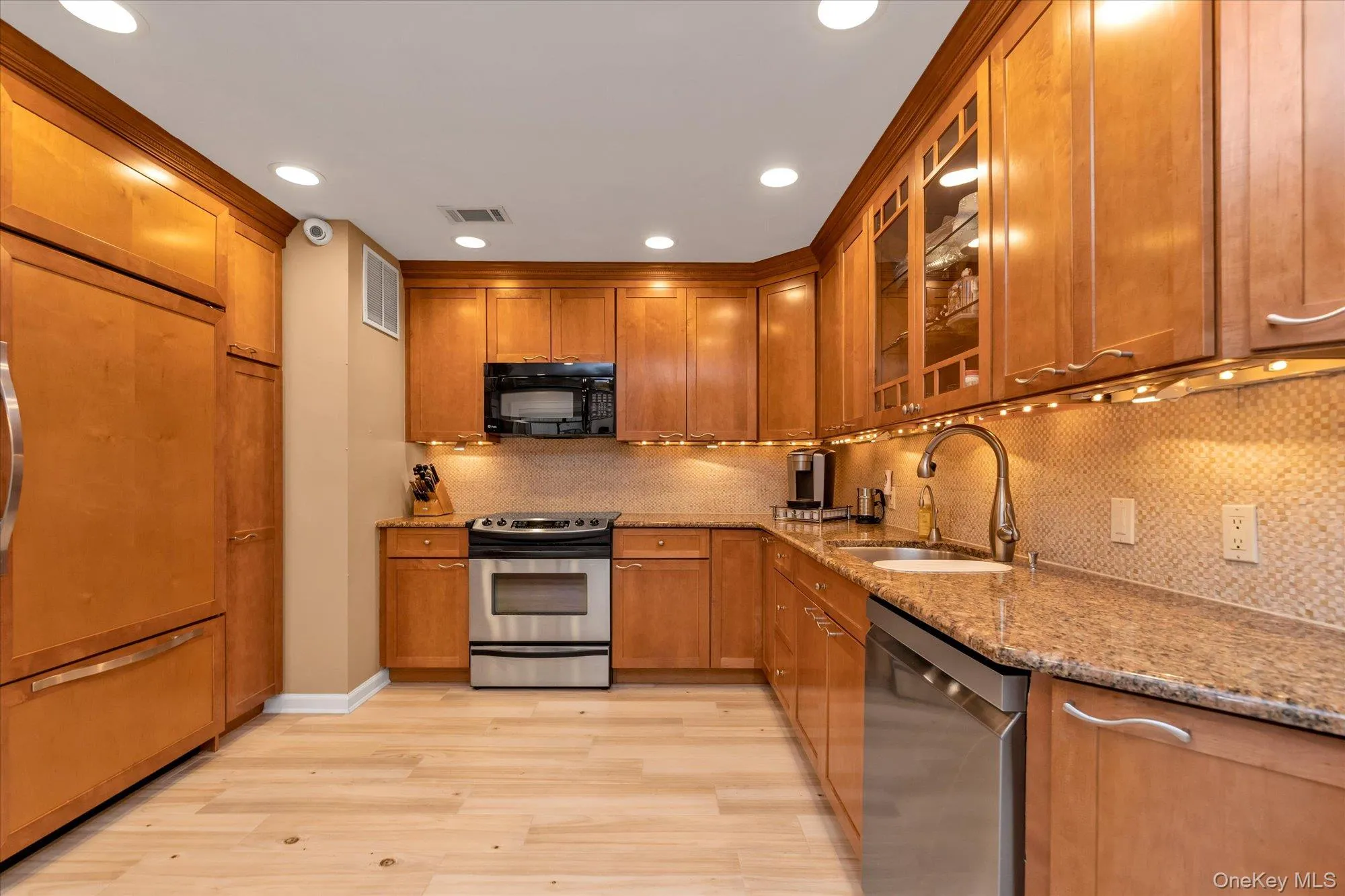 Kitchen featuring wood cabinetry, stainless steel appliances, granite countertops, and a tiled backsplash Kitchen featuring wood cabinetry, stainless steel appliances, granite countertops, and a tiled backsplash