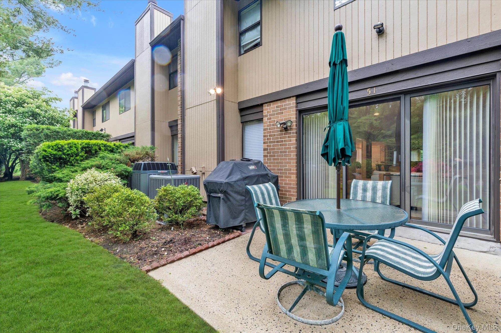Concrete patio with a sliding glass door entry, bordered by manicured landscaping and a grass lawn Concrete patio with a sliding glass door entry, bordered by manicured landscaping and a grass lawn