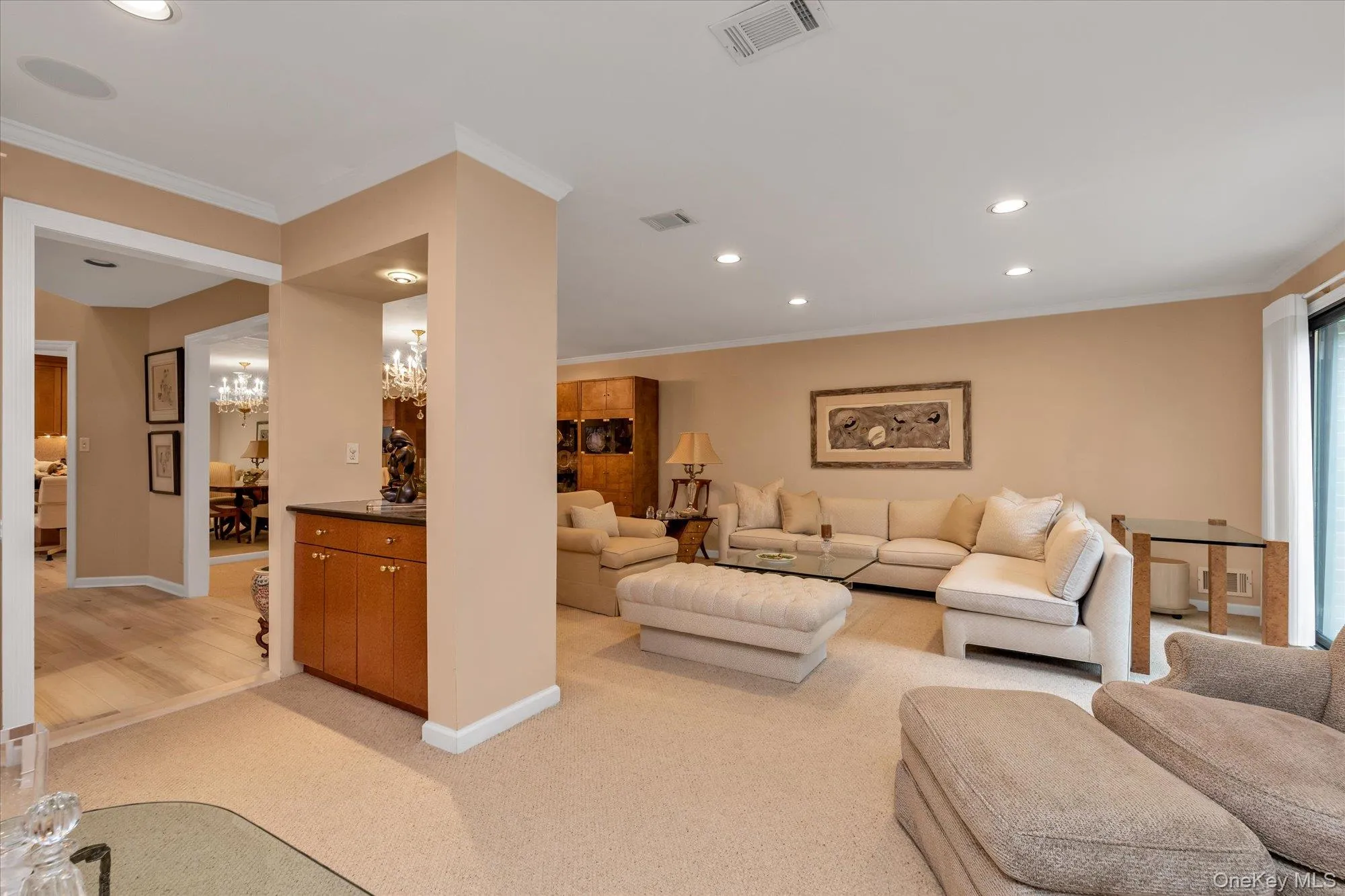 Spacious living area featuring neutral carpeting, recessed lighting, crown molding, a built-in bar with wood cabinetry and a dark countertop, and a large sliding glass door Spacious living area featuring neutral carpeting, recessed lighting, crown molding, a built-in bar with wood cabinetry and a dark countertop, and a large sliding glass door