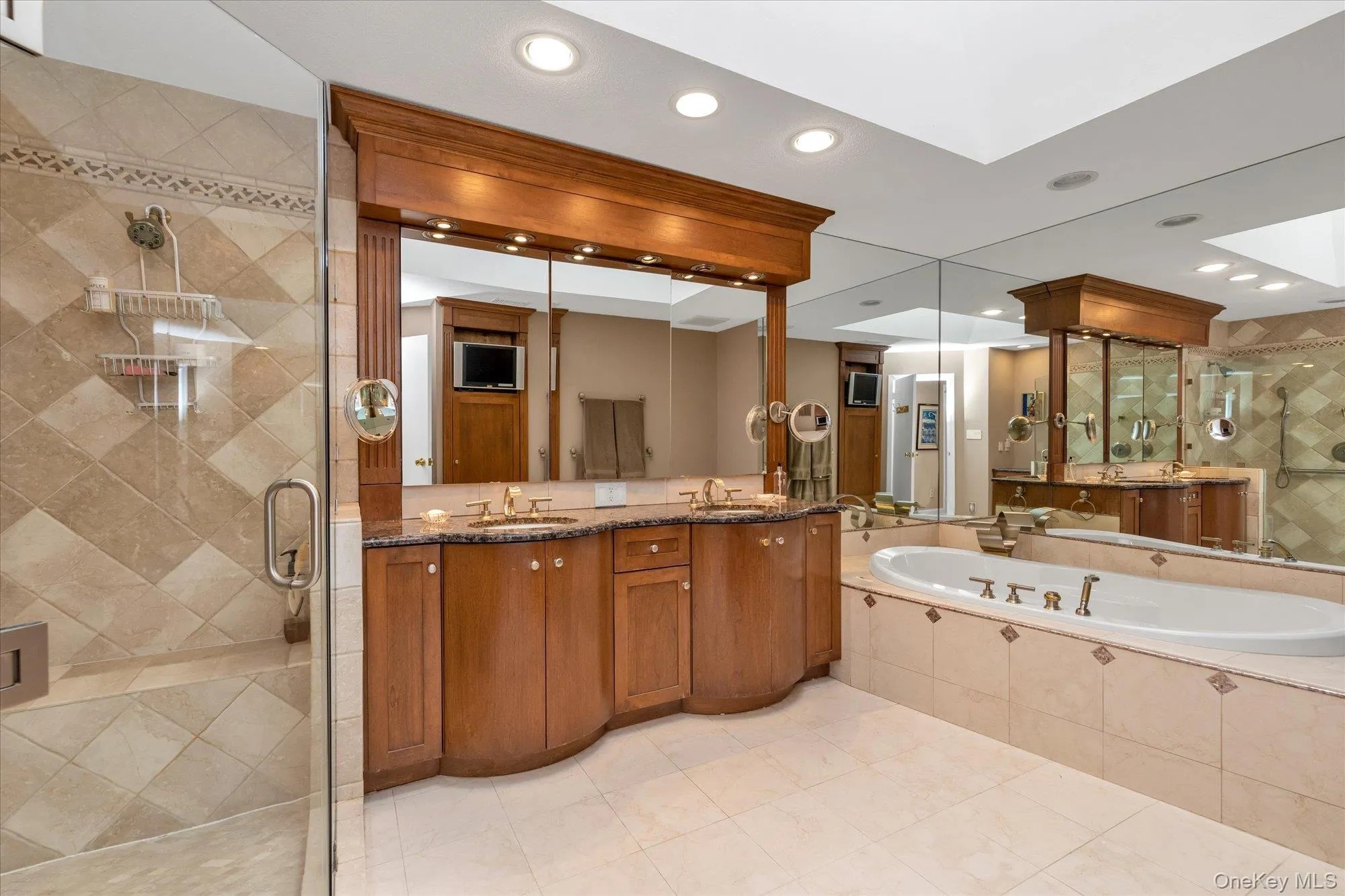 Primary bathroom featuring an Ultra Bath whirlpool bathtub, a Roman Waterfall faucet, a dual vanity with a marble countertop, undermount sinks, and brass-tone fixtures Primary bathroom featuring an Ultra Bath whirlpool bathtub, a Roman Waterfall faucet, a dual vanity with a marble countertop, undermount sinks, and brass-tone fixtures
