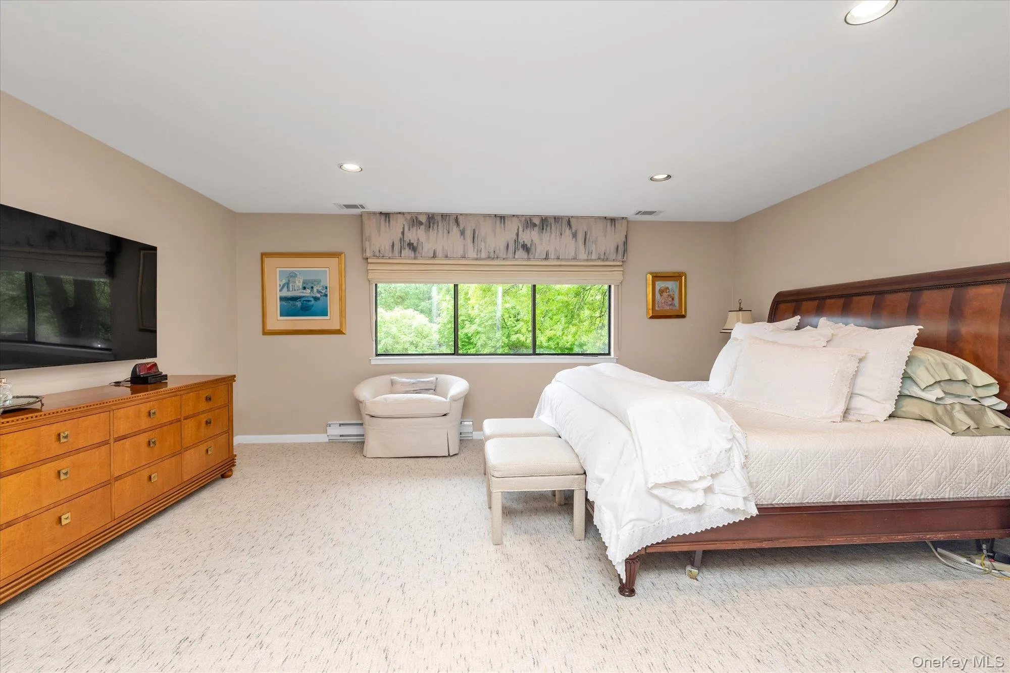 Primary bedroom featuring a large window with a patterned valance, recessed lighting, carpeting and neutral wall tones Primary bedroom featuring a large window with a patterned valance, recessed lighting, carpeting and neutral wall tones