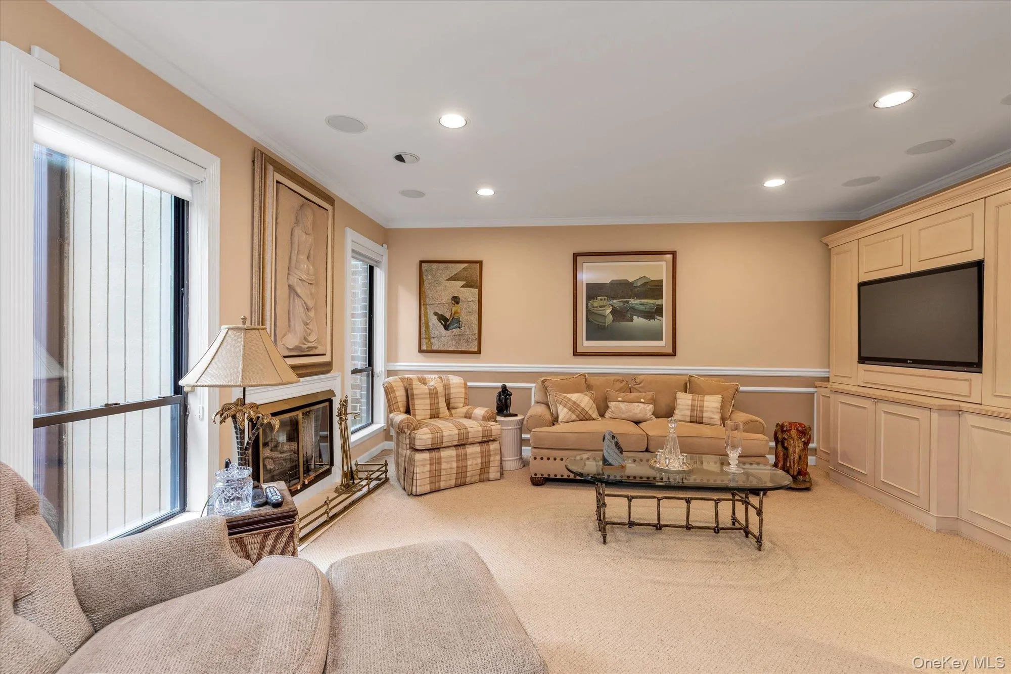 Living space featuring a built-in media center with panel cabinetry, recessed lighting, crown molding, a fireplace with a decorative mantel, and light-colored carpeting Living space featuring a built-in media center with panel cabinetry, recessed lighting, crown molding, a fireplace with a decorative mantel, and light-colored carpeting