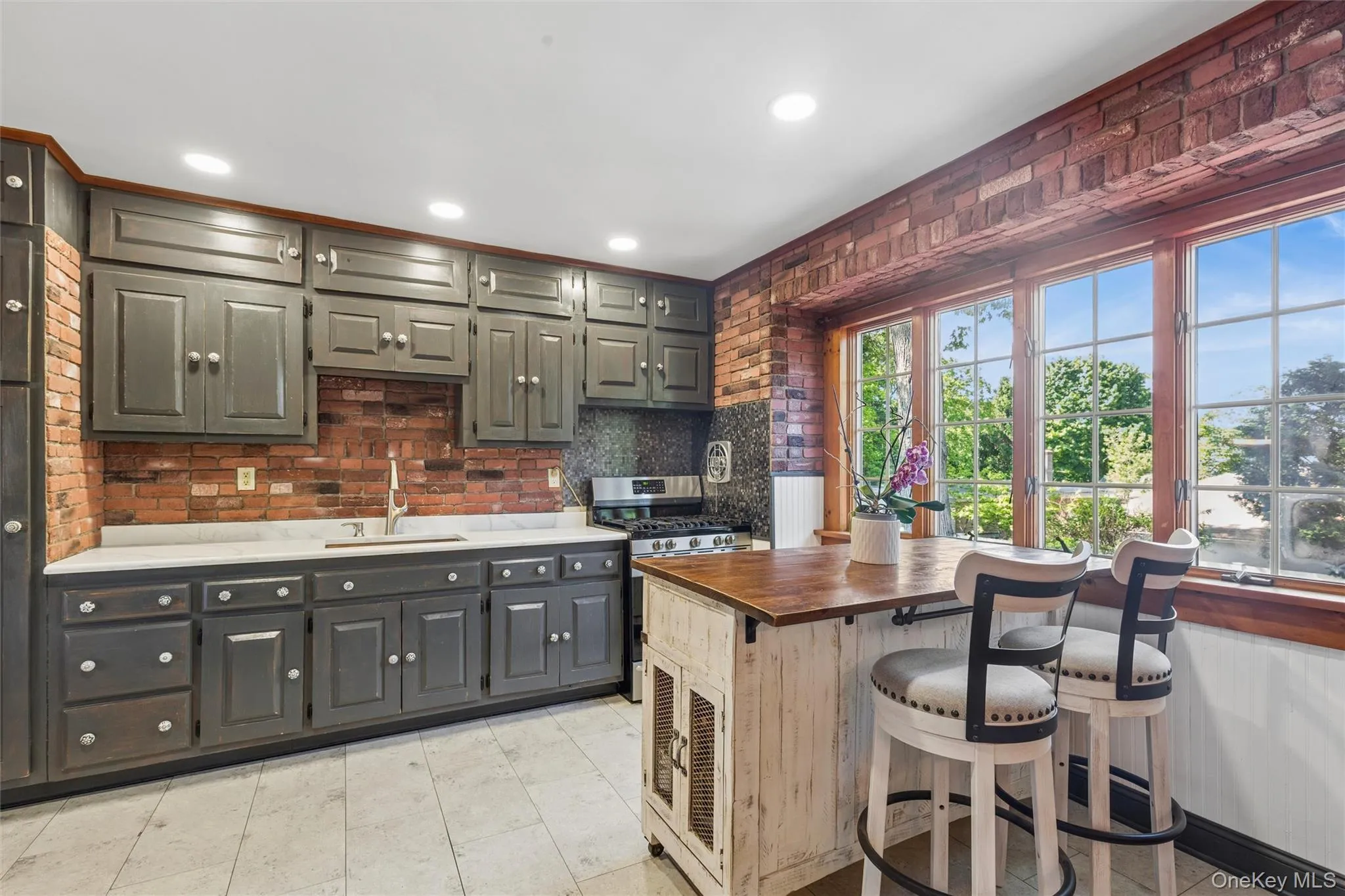 Eat in kitchen with detailed wood cabinetry, brick accent walls, tile flooring, quartz countertops, and a built-in oven range Eat in kitchen with detailed wood cabinetry, brick accent walls, tile flooring, quartz countertops, and a built-in oven range