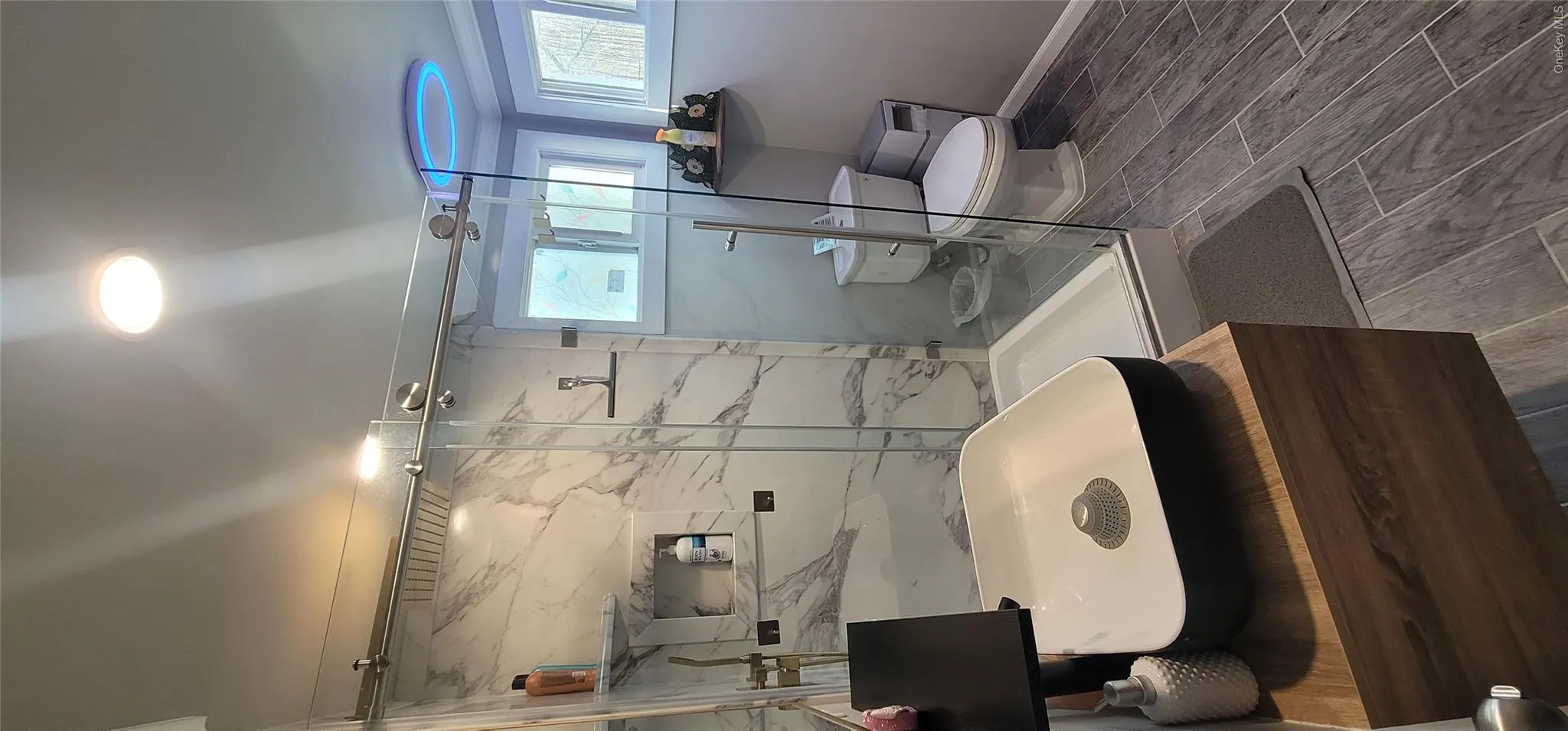 Full bathroom with a wealth of natural light, toilet, a marble finish shower, and baseboards Full bathroom with a wealth of natural light, toilet, a marble finish shower, and baseboards