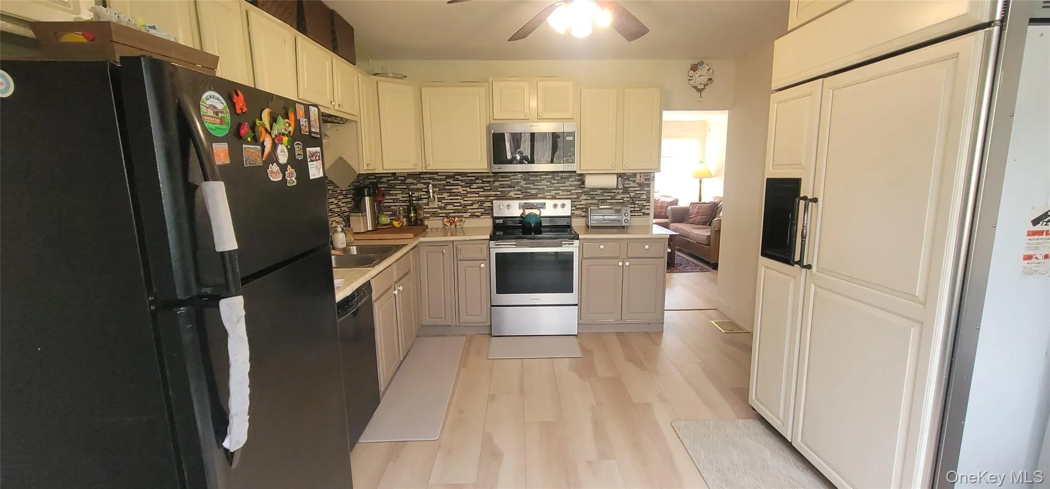 Kitchen featuring stainless steel appliances, light wood finished floors, light countertops, decorative backsplash, and a ceiling fan Kitchen featuring stainless steel appliances, light wood finished floors, light countertops, decorative backsplash, and a ceiling fan