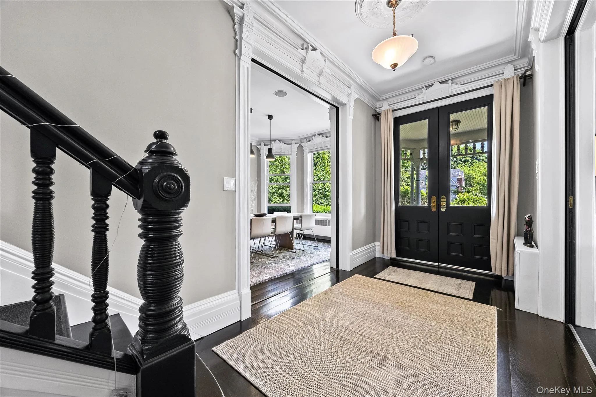 Grand foyer featuring dark wood-finish flooring and a black painted staircase with decorative newel post Grand foyer featuring dark wood-finish flooring and a black painted staircase with decorative newel post