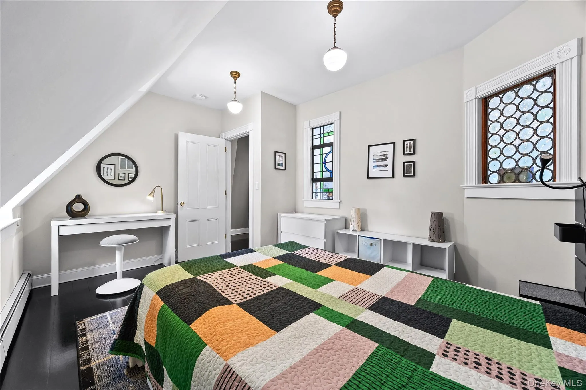 Bedroom featuring dark wood-finish flooring, two decorative stained-glass windows, sloped ceiling detail, and built-in shelving Bedroom featuring dark wood-finish flooring, two decorative stained-glass windows, sloped ceiling detail, and built-in shelving