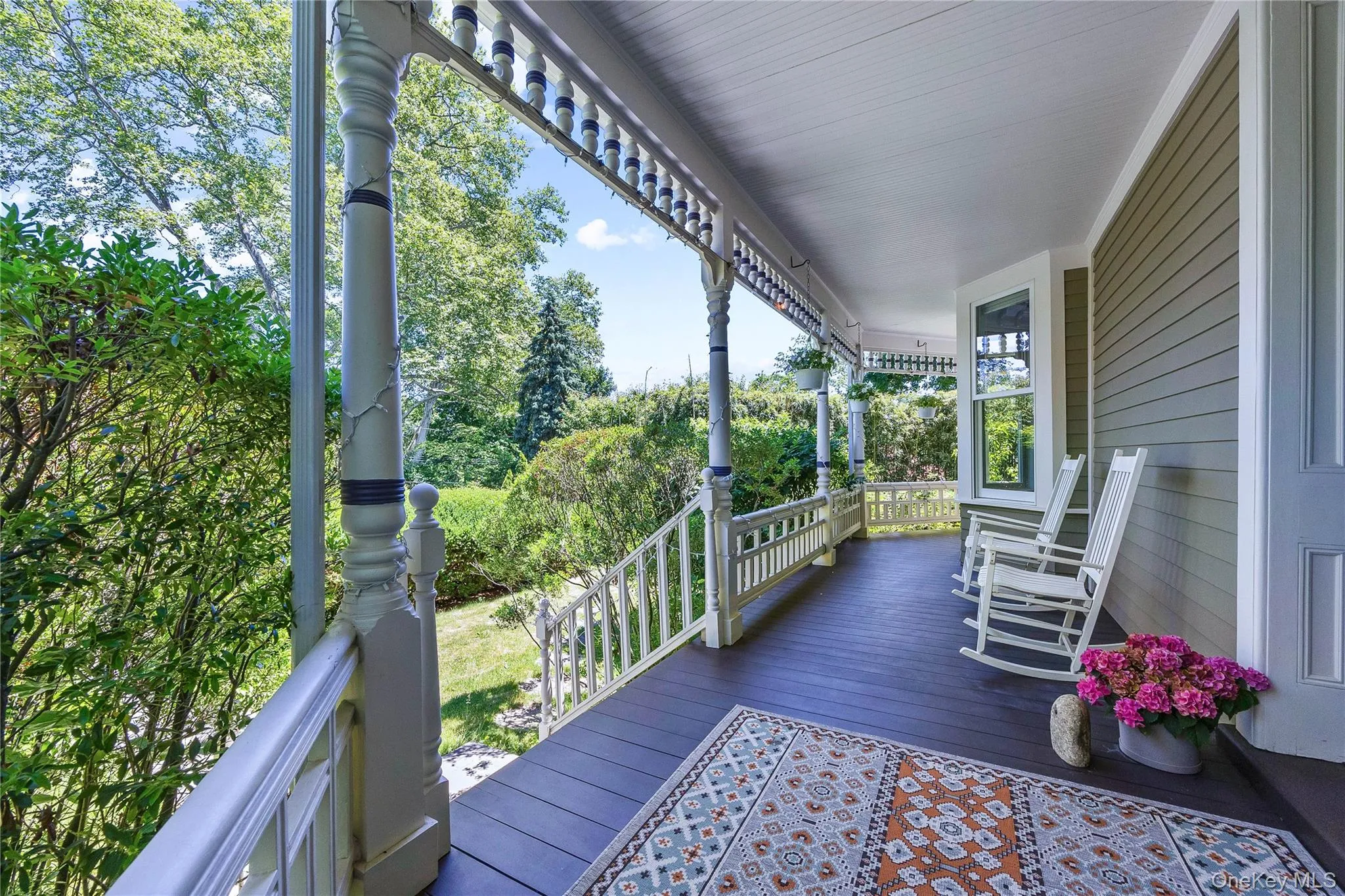 Expansive covered porch with dark wood-finish flooring, decorative white balustrade, and a beadboard ceiling Expansive covered porch with dark wood-finish flooring, decorative white balustrade, and a beadboard ceiling