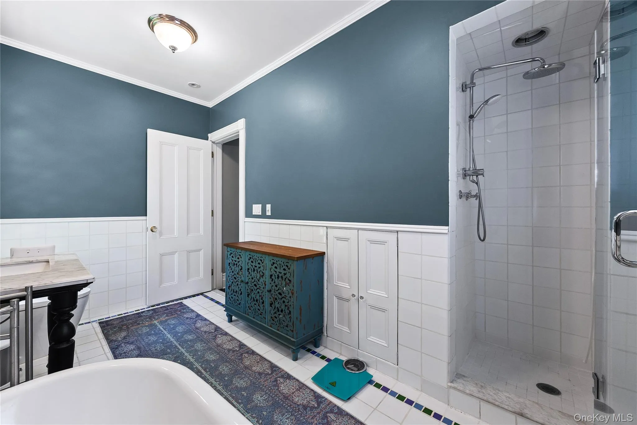 Bathroom featuring a large glass-enclosed shower with a rainfall showerhead, white subway tile wainscoting, and a freestanding soaking tub Bathroom featuring a large glass-enclosed shower with a rainfall showerhead, white subway tile wainscoting, and a freestanding soaking tub