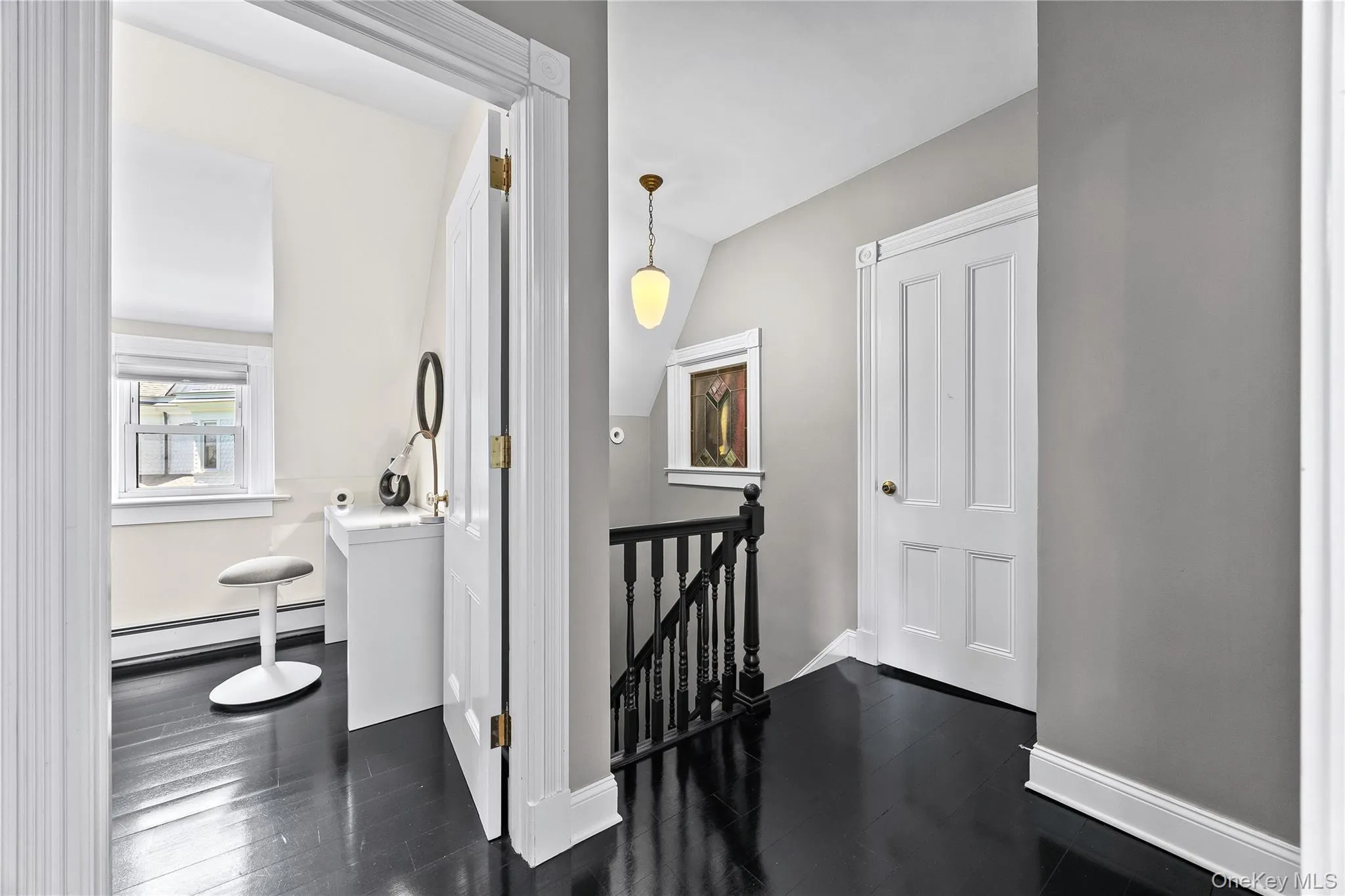 Third-level hallway featuring dark wood-finish flooring, a white paneled door, and a traditional spindle railing Third-level hallway featuring dark wood-finish flooring, a white paneled door, and a traditional spindle railing