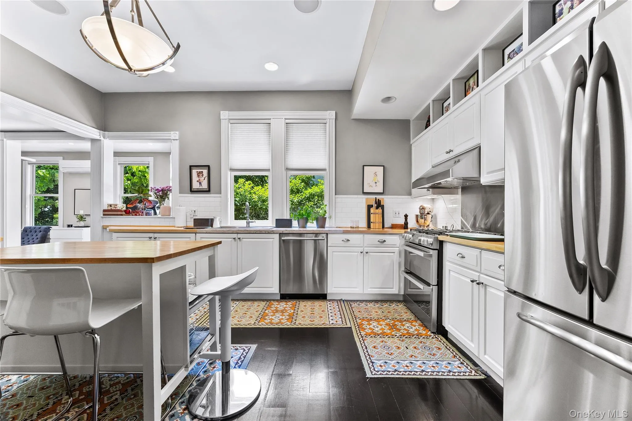 Kitchen featuring dark wood-finish flooring, white cabinetry, light wood-finish countertops, stainless steel appliances, and a white subway tile backsplash Kitchen featuring dark wood-finish flooring, white cabinetry, light wood-finish countertops, stainless steel appliances, and a white subway tile backsplash