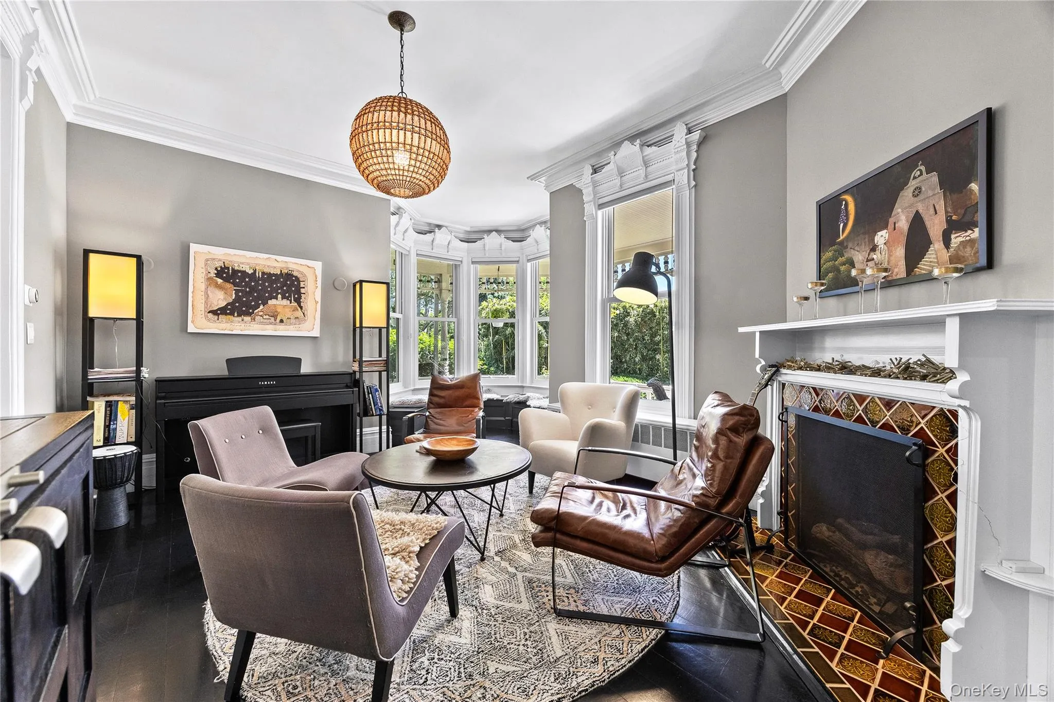 Living area featuring dark wood-finish flooring, a decorative fireplace with patterned tile surround, and a bay window Living area featuring dark wood-finish flooring, a decorative fireplace with patterned tile surround, and a bay window