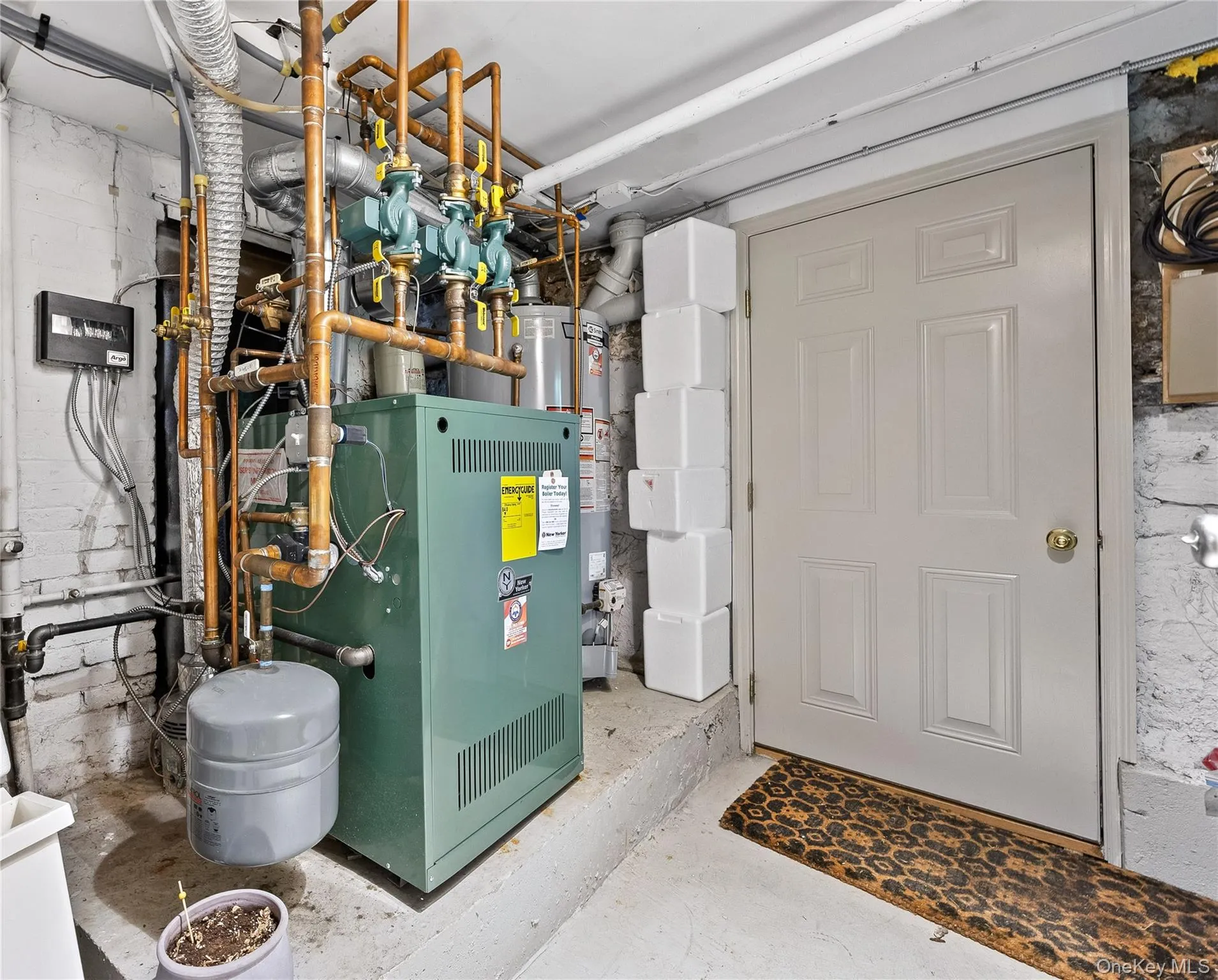 Utility room featuring a modern boiler system with copper piping, an adjacent water heater, and a paneled interior door with a brass-finish doorknob Utility room featuring a modern boiler system with copper piping, an adjacent water heater, and a paneled interior door with a brass-finish doorknob