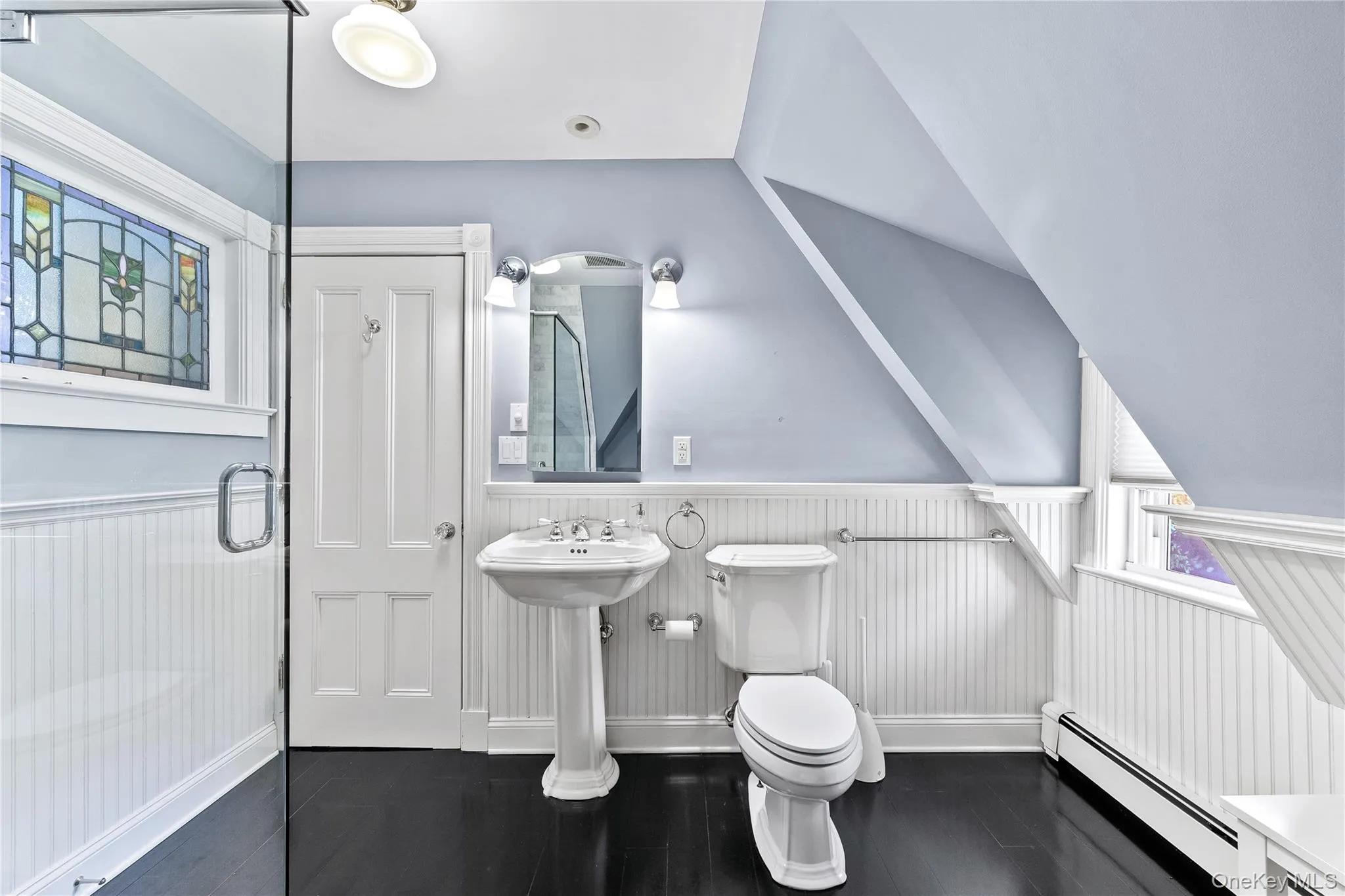 Bathroom featuring a pedestal sink, white toilet, and dark wood-finish flooring Bathroom featuring a pedestal sink, white toilet, and dark wood-finish flooring