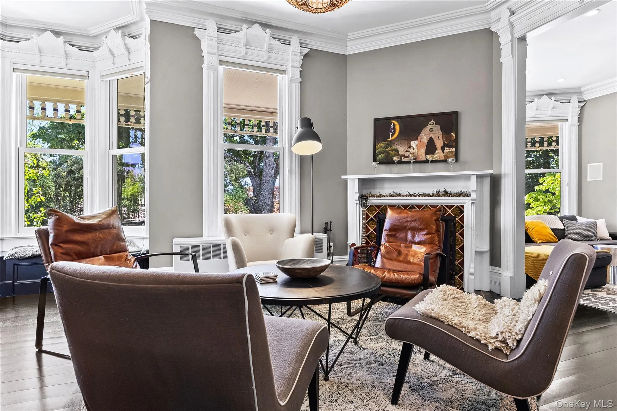 Living area featuring dark wood-finish flooring, a decorative fireplace with patterned tile surround, and a bay window Living area featuring dark wood-finish flooring, a decorative fireplace with patterned tile surround, and a bay window