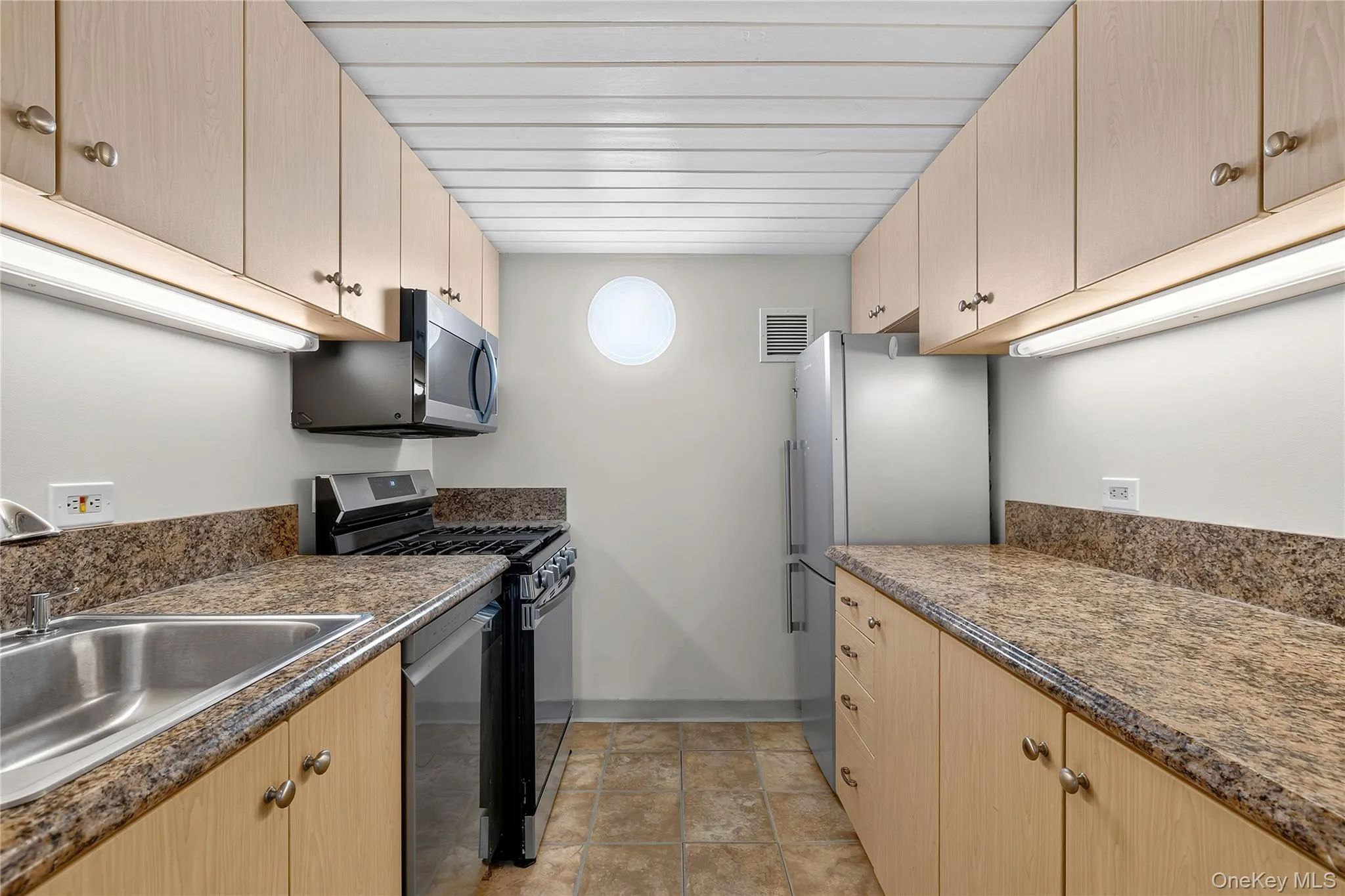 Galley kitchen featuring light wood-finish cabinetry, granite-patterned countertops, and tile flooring Galley kitchen featuring light wood-finish cabinetry, granite-patterned countertops, and tile flooring