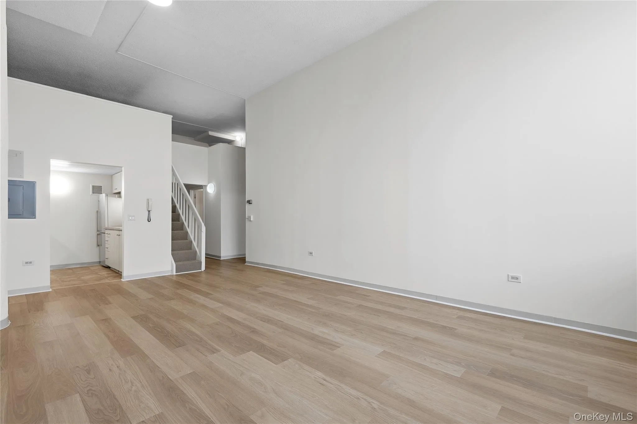 Open-concept living space featuring wood-finish flooring, high ceilings, a prominent structural column, and a modern staircase with a carpet runner Open-concept living space featuring wood-finish flooring, high ceilings, a prominent structural column, and a modern staircase with a carpet runner