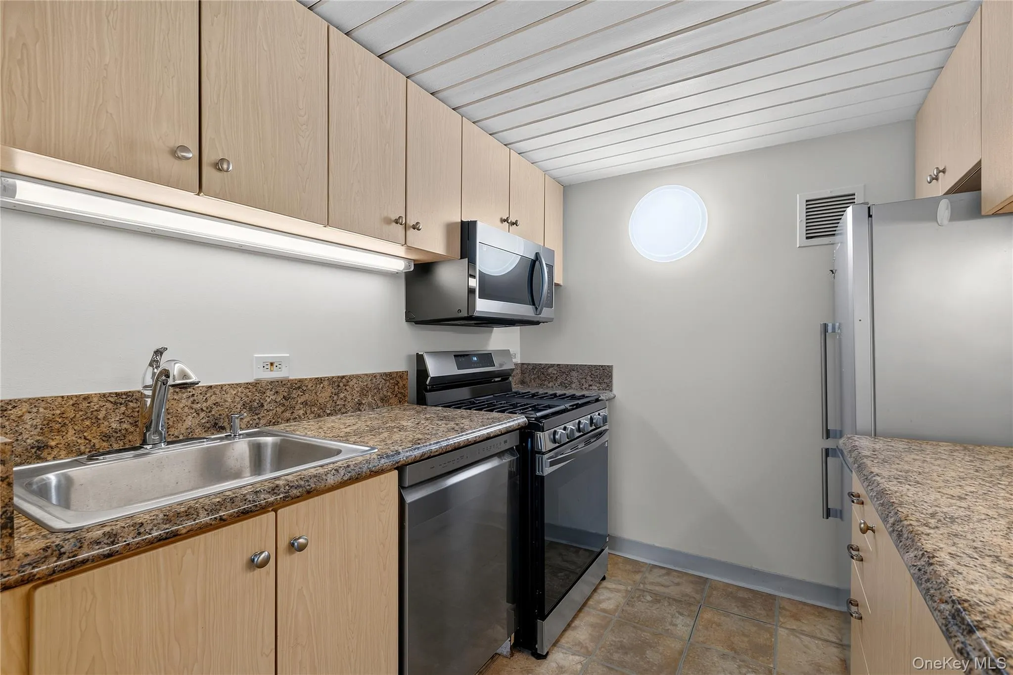 Kitchen featuring wood-finish cabinetry, granite-style countertops, stainless steel sink, and tile flooring Kitchen featuring wood-finish cabinetry, granite-style countertops, stainless steel sink, and tile flooring