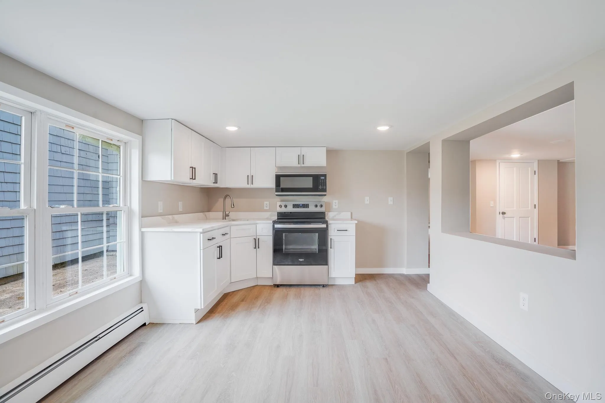 Modern kitchen featuring white shaker-style cabinetry with matte black hardware, stainless steel appliances, and light wood-finish flooring Modern kitchen featuring white shaker-style cabinetry with matte black hardware, stainless steel appliances, and light wood-finish flooring
