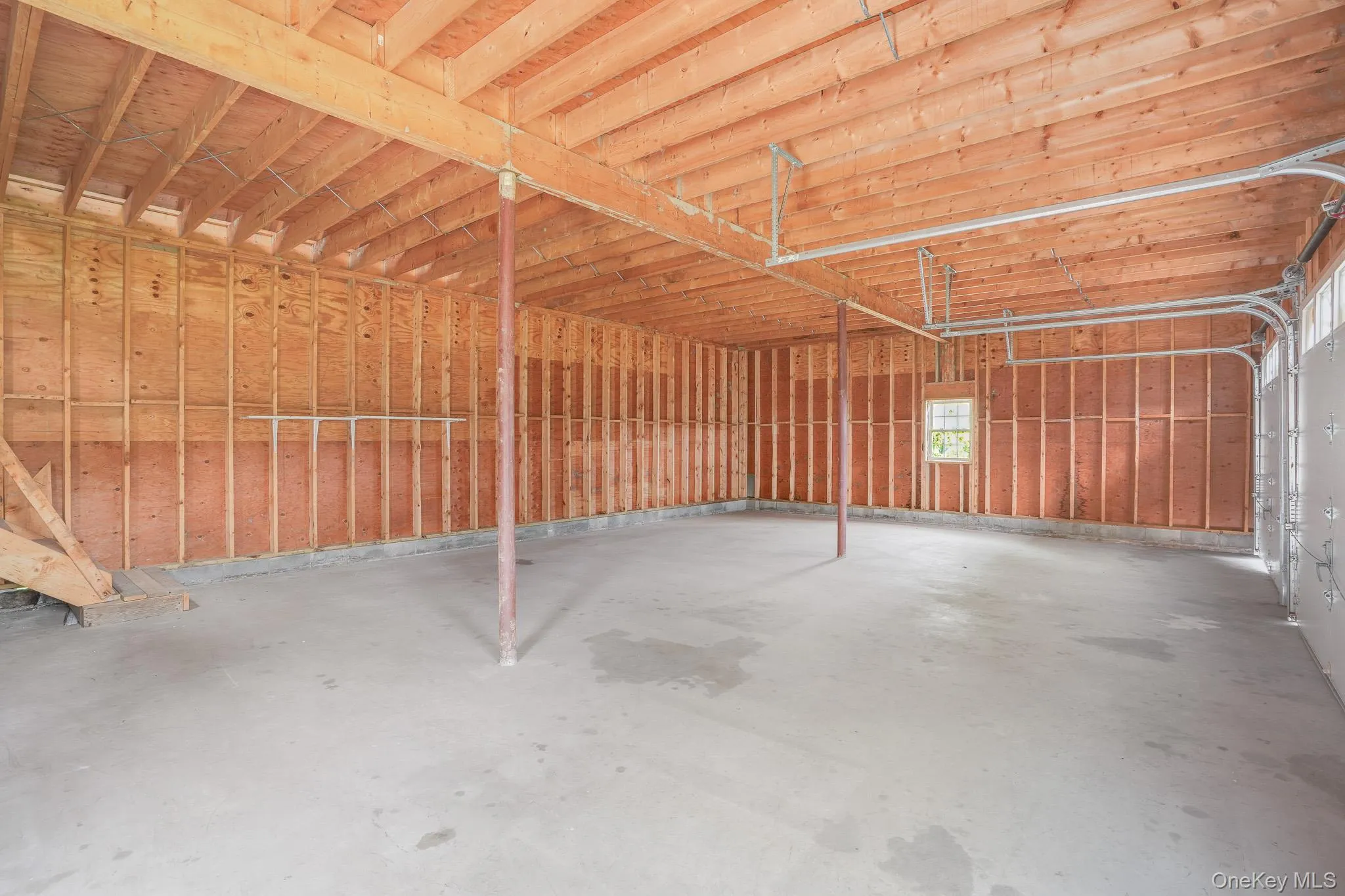 Spacious two-car garage featuring a concrete floor, exposed wood framing, and an overhead garage door track system Spacious two-car garage featuring a concrete floor, exposed wood framing, and an overhead garage door track system