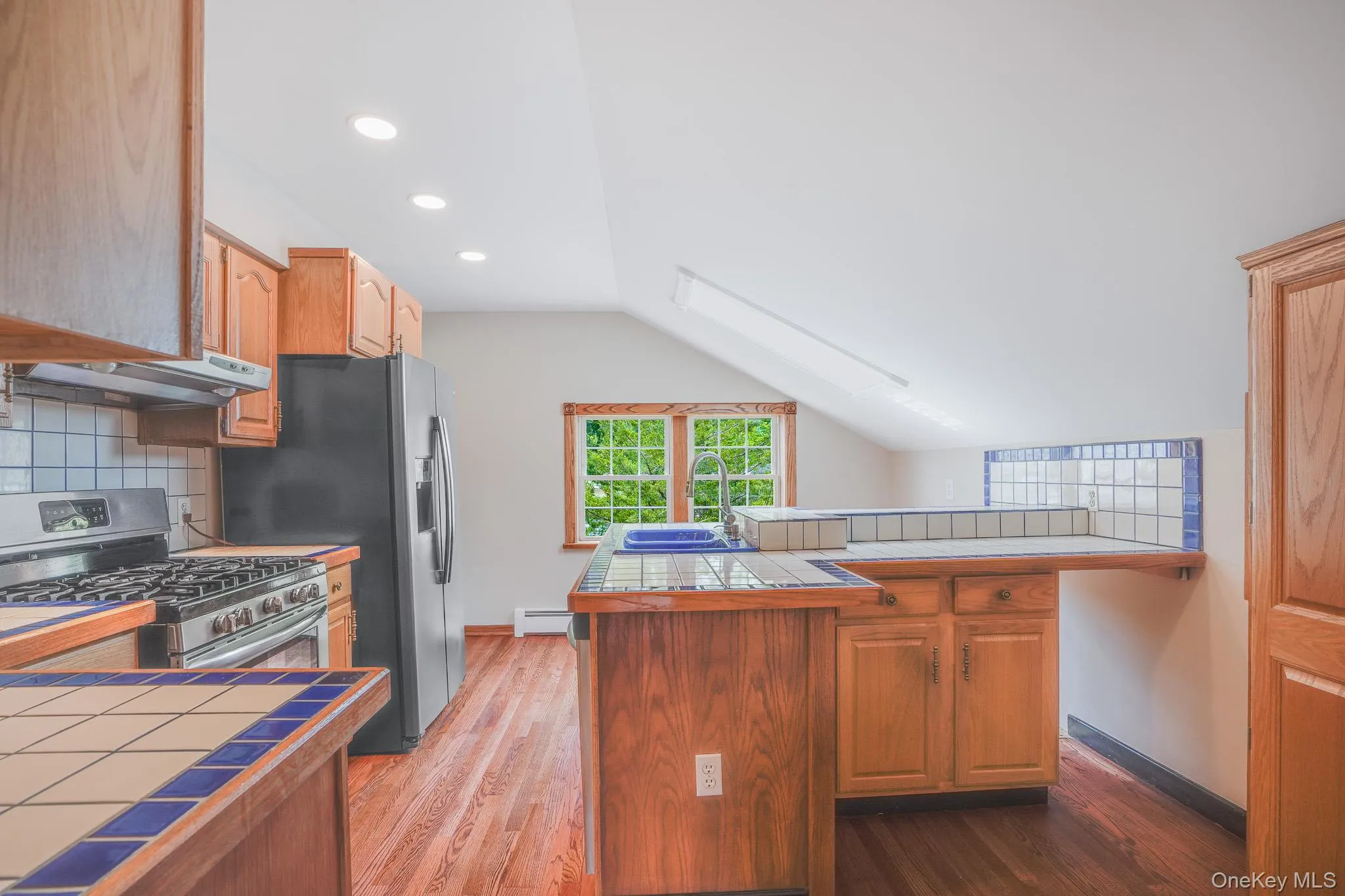 Kitchen featuring wood-finish flooring, recessed lighting, and a window overlooking greenery Kitchen featuring wood-finish flooring, recessed lighting, and a window overlooking greenery
