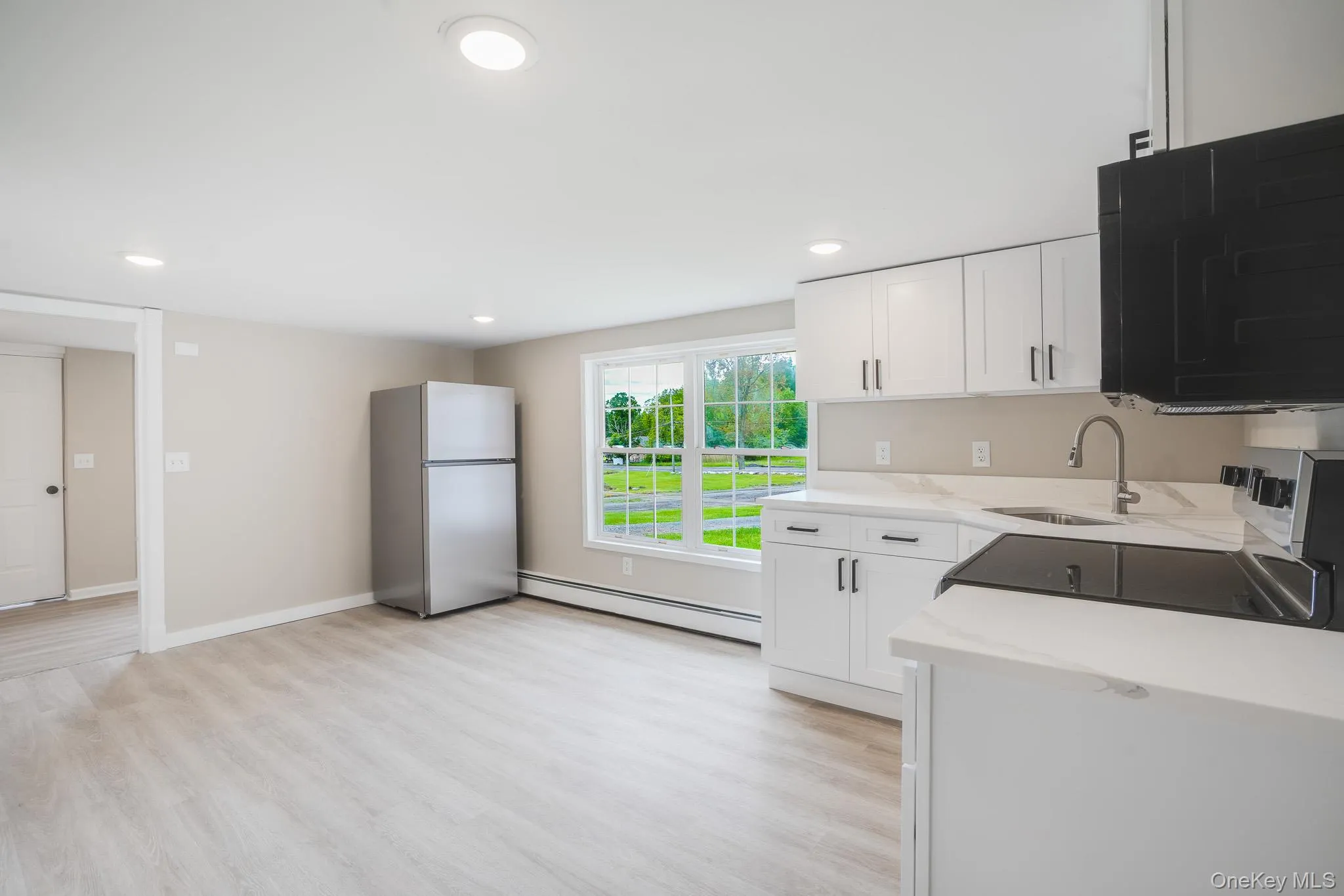 Kitchen featuring white cabinetry, light-toned countertops, stainless steel appliances, and wood-finish flooring Kitchen featuring white cabinetry, light-toned countertops, stainless steel appliances, and wood-finish flooring