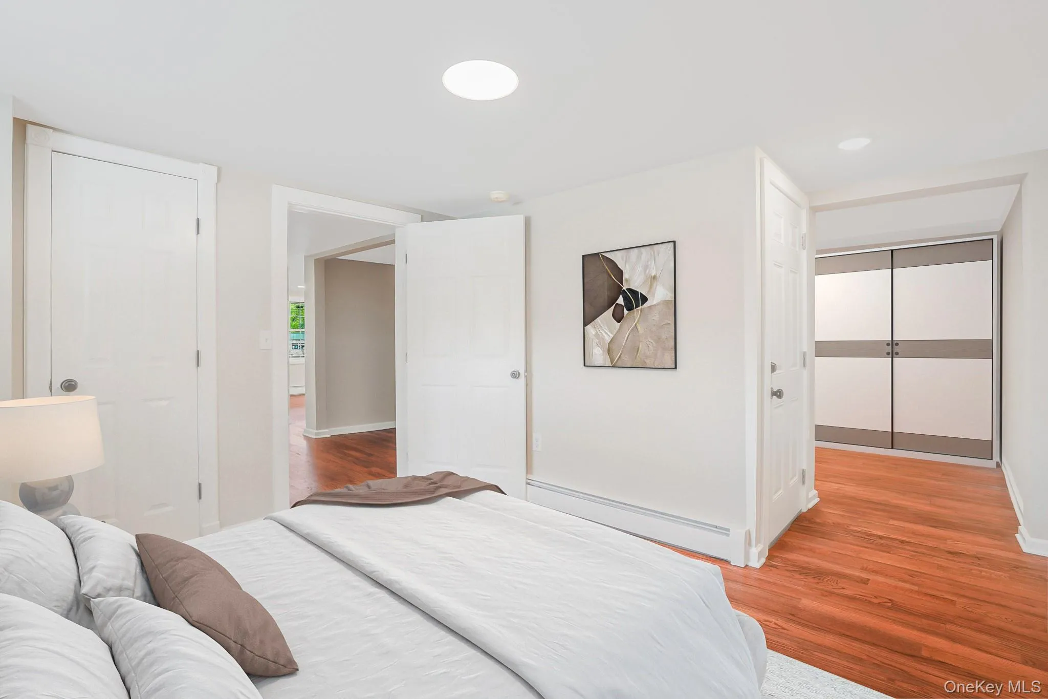 Bright white interior featuring wood-finish flooring, white baseboards, and a built-in closet with sliding panel doors Bright white interior featuring wood-finish flooring, white baseboards, and a built-in closet with sliding panel doors