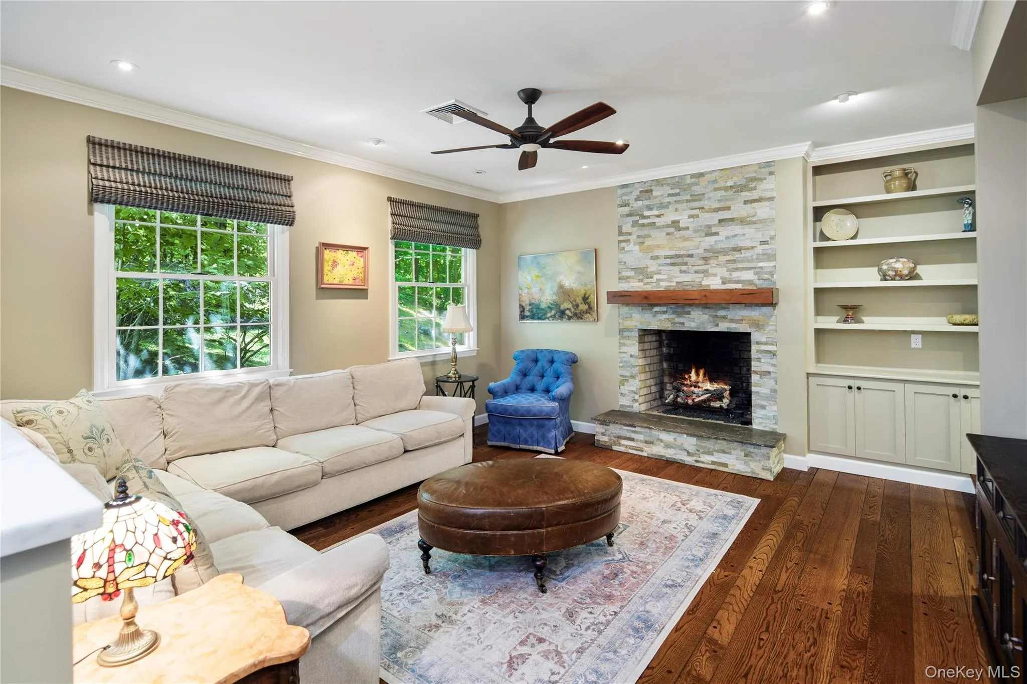 The living room features a raised hearth fireplace with stacked stone floor to ceiling surround and thick wood mantle shelf, flanked by built-in cabinetry and shelving, recessed eyeball lighting, a ceiling fan, crown molding and refinished pegged wide board oak floors. Opens directly onto newly renovated eat-in kitchen and dining area. The living room features a raised hearth fireplace with stacked stone floor to ceiling surround and thick wood mantle shelf, flanked by built-in cabinetry and shelving, recessed eyeball lighting, a ceiling fan, crown molding and refinished pegged wide board oak floors. Opens directly onto newly renovated eat-in kitchen and dining area.