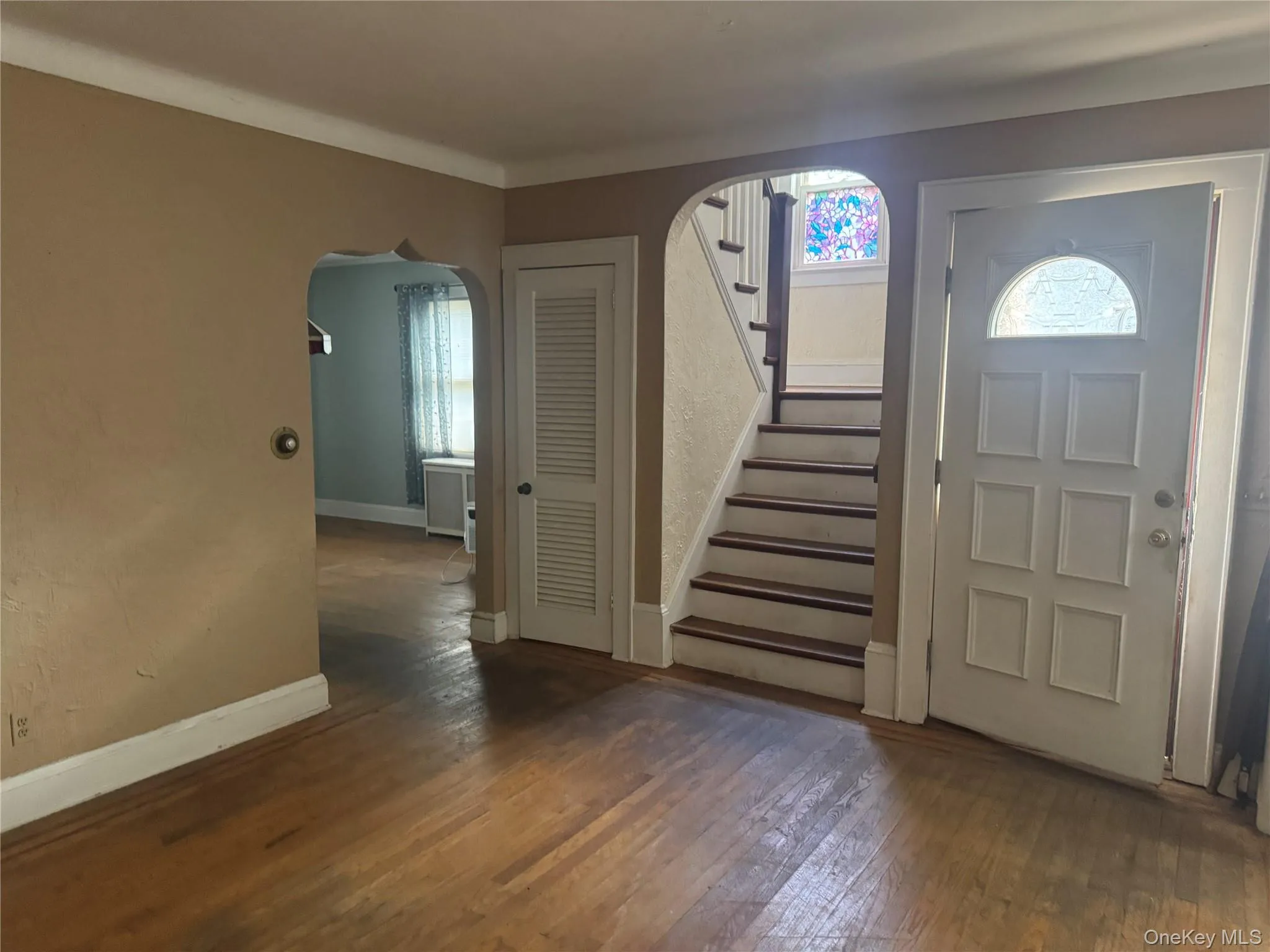 Hardwood flooring extends throughout the entry, featuring a decorative front door with an arched window Hardwood flooring extends throughout the entry, featuring a decorative front door with an arched window