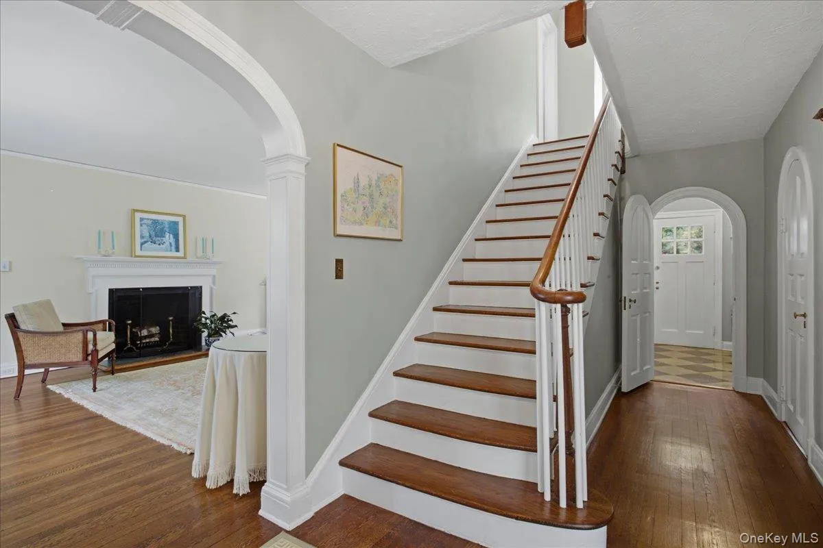 Entry hall featuring a wood-finish staircase with white risers and balusters, arched doorways, a coat closet, and wood-finish flooring Entry hall featuring a wood-finish staircase with white risers and balusters, arched doorways, a coat closet, and wood-finish flooring