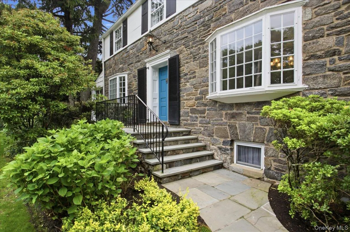 Stone exterior residence featuring a vibrant blue entry door, an elegant bay window, and a bluestone walkway Stone exterior residence featuring a vibrant blue entry door, an elegant bay window, and a bluestone walkway