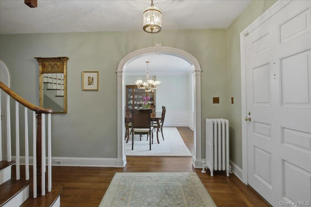 Entryway featuring hardwood flooring, an arched doorway, with view of the DR, curved staircase with wood railing, and a decorative ceiling light fixture Entryway featuring hardwood flooring, an arched doorway, with view of the DR, curved staircase with wood railing, and a decorative ceiling light fixture