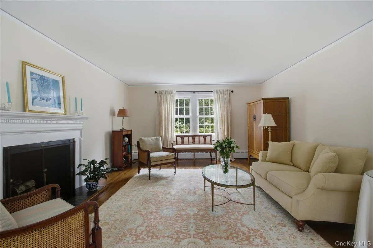 Living area featuring a white mantel fireplace with a black firebox, wood-finish flooring, white trim, and a window with multiple panes Living area featuring a white mantel fireplace with a black firebox, wood-finish flooring, white trim, and a window with multiple panes