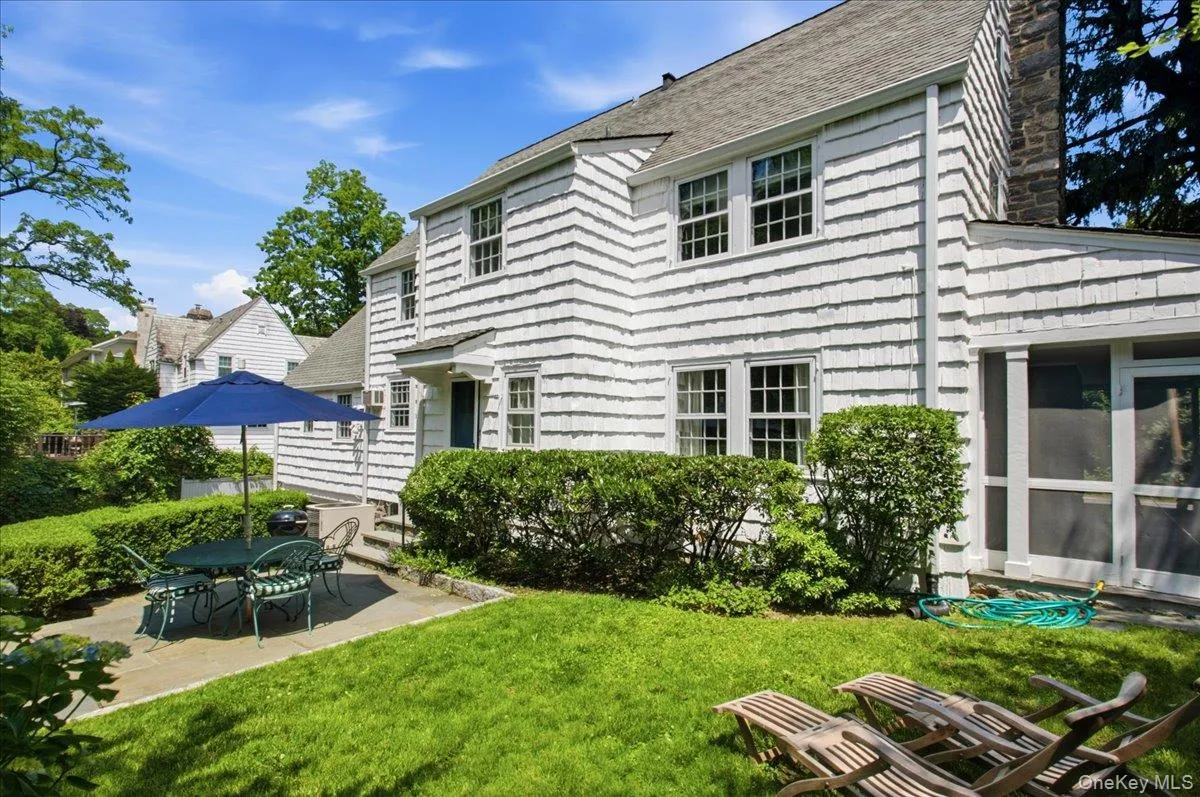 White shingle-sided exterior with a stone chimney and multiple windows and screened porch on the right. White shingle-sided exterior with a stone chimney and multiple windows and screened porch on the right.