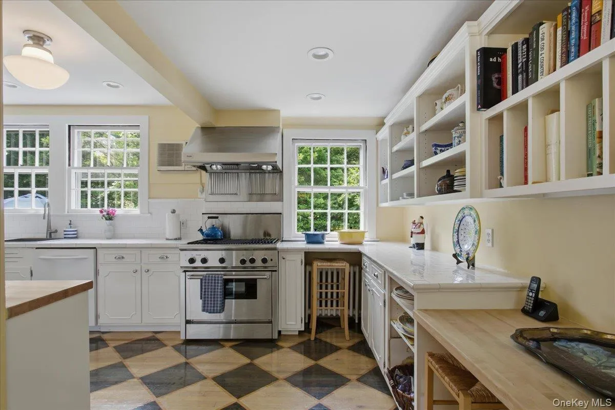 Kitchen featuring checkerboard flooring, wall of shelving, white cabinetry, and multiple windows Kitchen featuring checkerboard flooring, wall of shelving, white cabinetry, and multiple windows