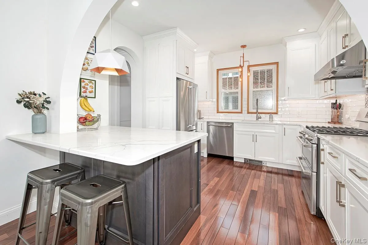 Kitchen featuring stainless steel appliances, under cabinet range hood, a sink, dark wood-style flooring, and white cabinets Kitchen featuring stainless steel appliances, under cabinet range hood, a sink, dark wood-style flooring, and white cabinets