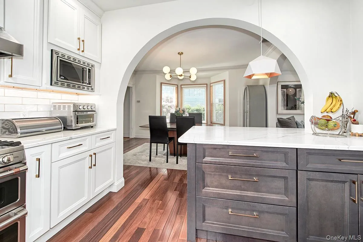 Kitchen with stainless steel appliances, a chandelier, white cabinets, dark wood finished floors, and tasteful backsplash Kitchen with stainless steel appliances, a chandelier, white cabinets, dark wood finished floors, and tasteful backsplash