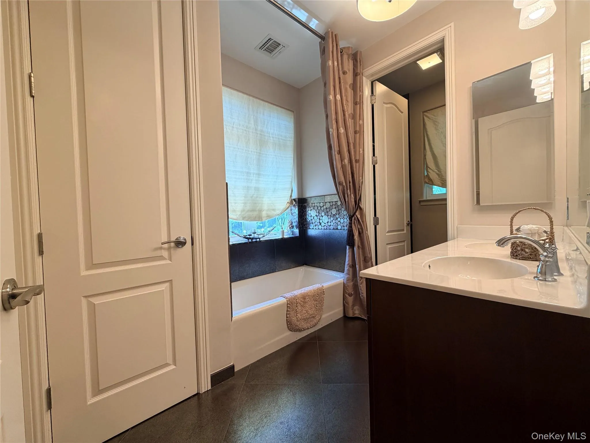 Bathroom featuring a double vanity with an integrated white sink and chrome faucet, white countertop, and dark wood-finish cabinetry Bathroom featuring a double vanity with an integrated white sink and chrome faucet, white countertop, and dark wood-finish cabinetry