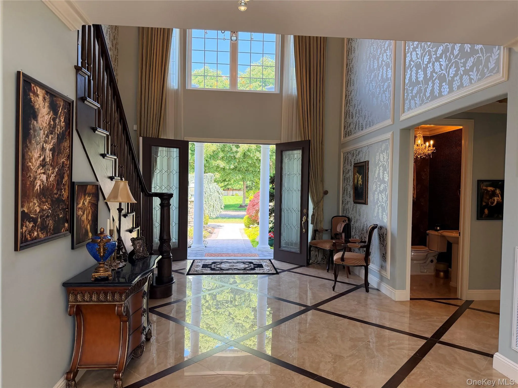 Two-story foyer featuring marble flooring with contrasting inlay, a dark wood staircase with ornate newel post, and decorative wall panels Two-story foyer featuring marble flooring with contrasting inlay, a dark wood staircase with ornate newel post, and decorative wall panels