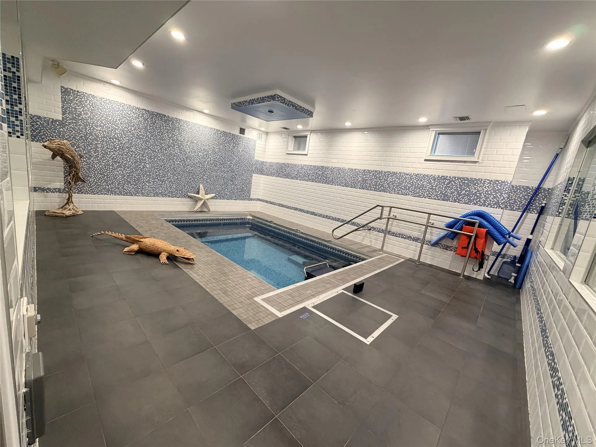 Indoor swimming pool featuring blue mosaic tile walls and dark gray floor tile Indoor swimming pool featuring blue mosaic tile walls and dark gray floor tile