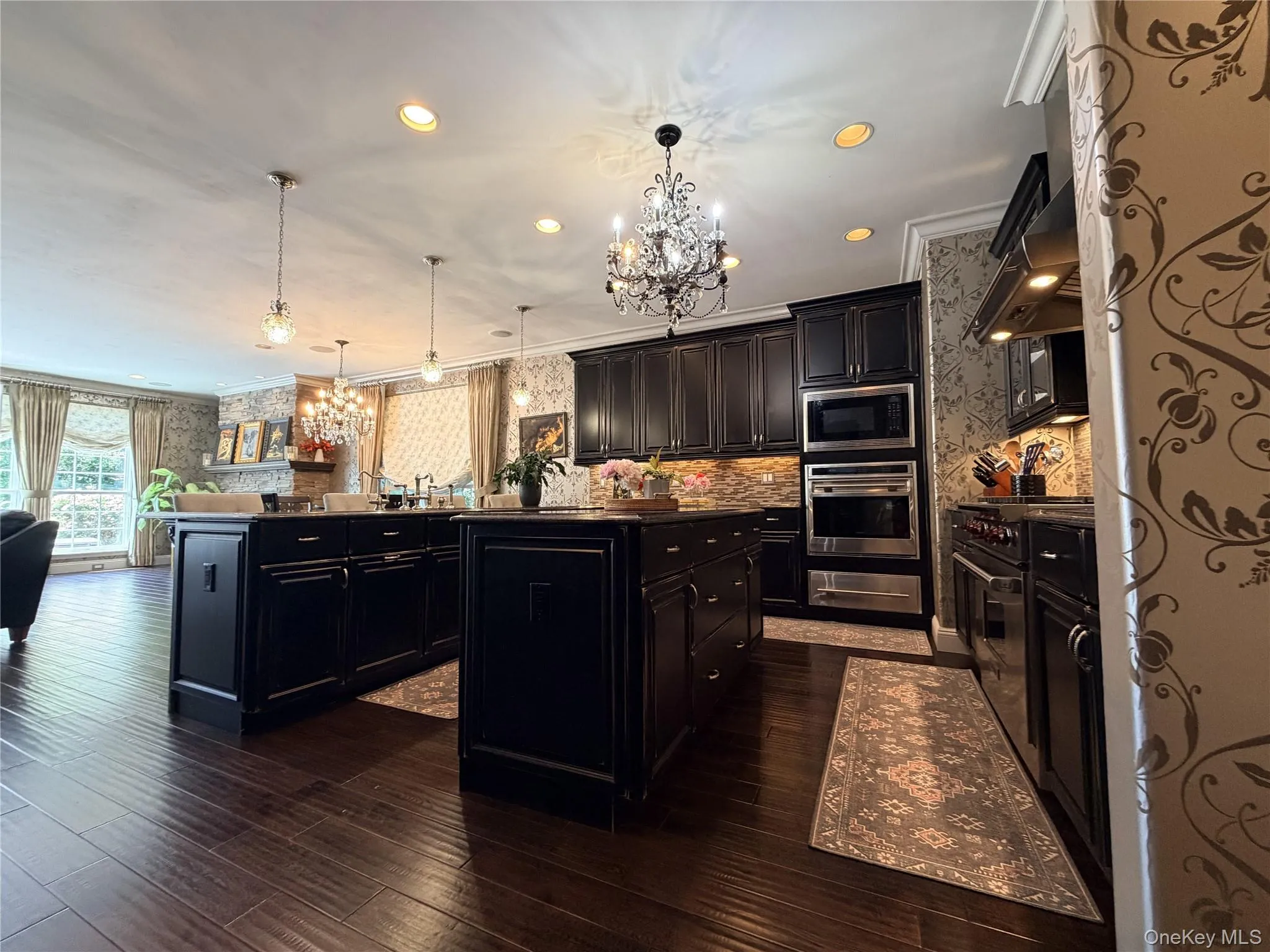 Kitchen featuring dark wood-finish flooring, two central islands, dark cabinetry, stainless steel appliances, and recessed lighting Kitchen featuring dark wood-finish flooring, two central islands, dark cabinetry, stainless steel appliances, and recessed lighting