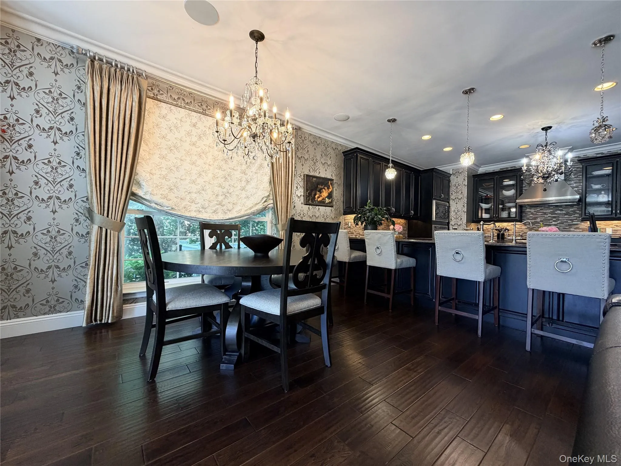 Open-concept space featuring dark wood-finish flooring, a kitchen with dark cabinetry, a breakfast bar, and a dining area with a chandelier Open-concept space featuring dark wood-finish flooring, a kitchen with dark cabinetry, a breakfast bar, and a dining area with a chandelier
