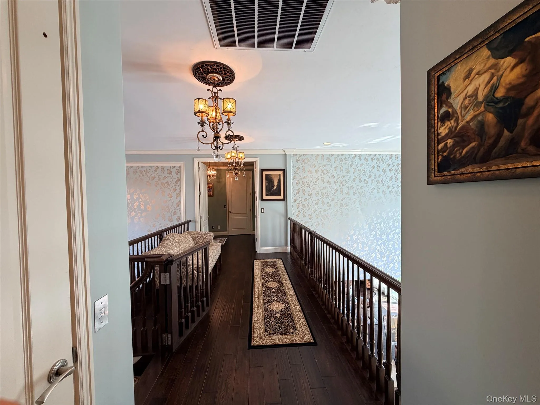 Upper-level hallway featuring dark wood-finish flooring, decorative wall paneling, and an ornate chandelier Upper-level hallway featuring dark wood-finish flooring, decorative wall paneling, and an ornate chandelier