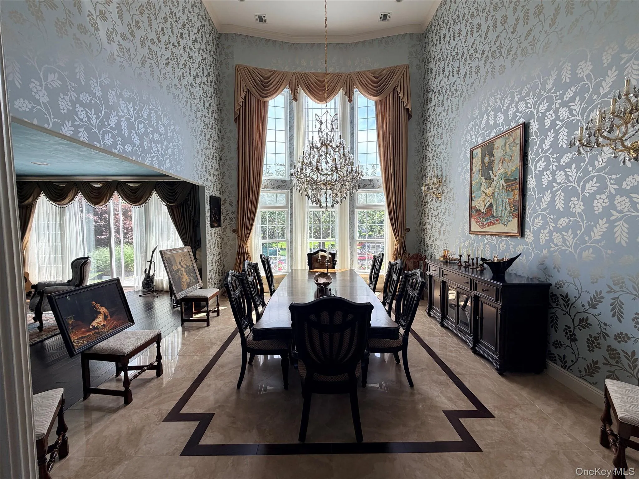 Dining space featuring a double-height ceiling, large windows with drapery, and patterned wallpaper Dining space featuring a double-height ceiling, large windows with drapery, and patterned wallpaper
